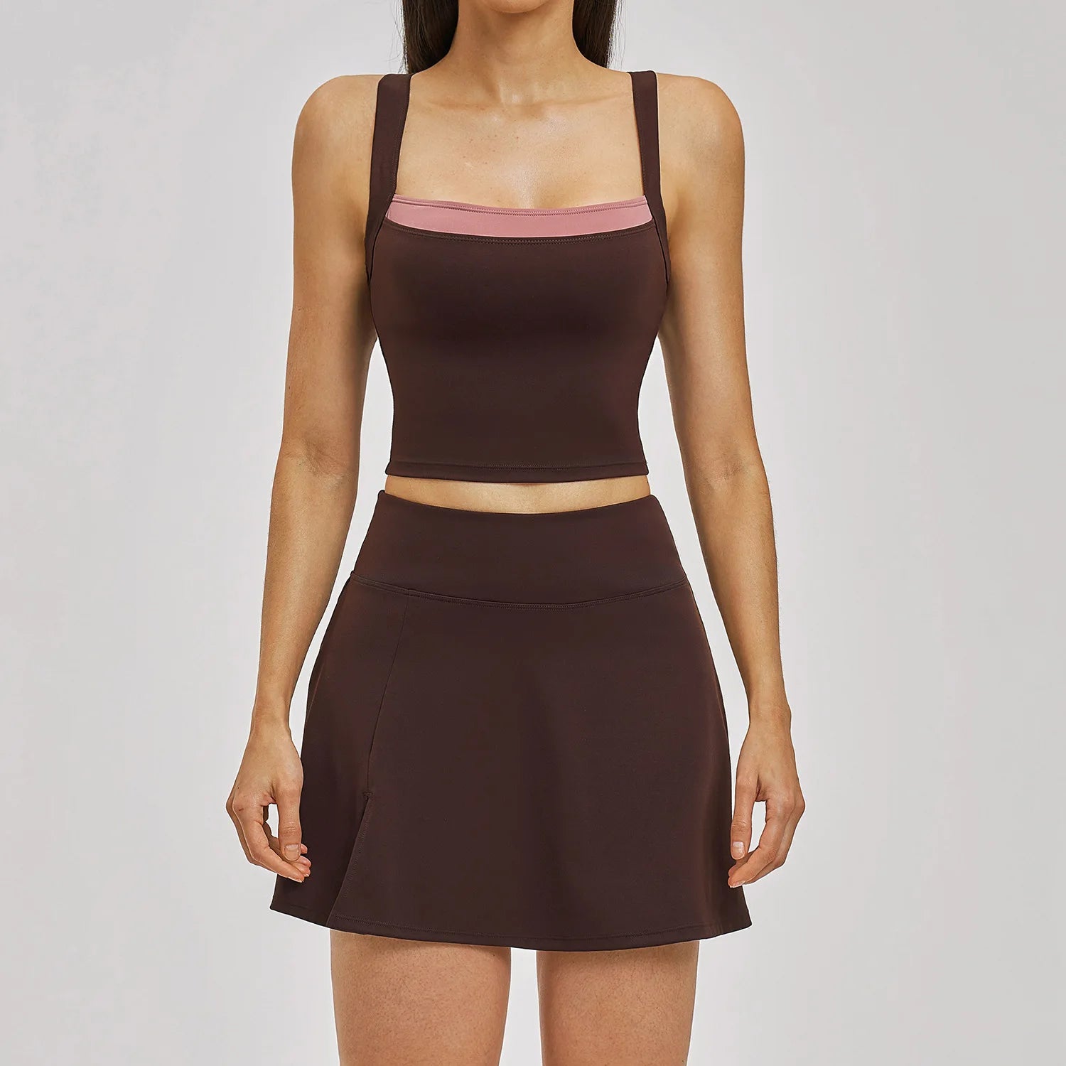 Woman wearing a brown athletic outfit with a skirt on a gray background