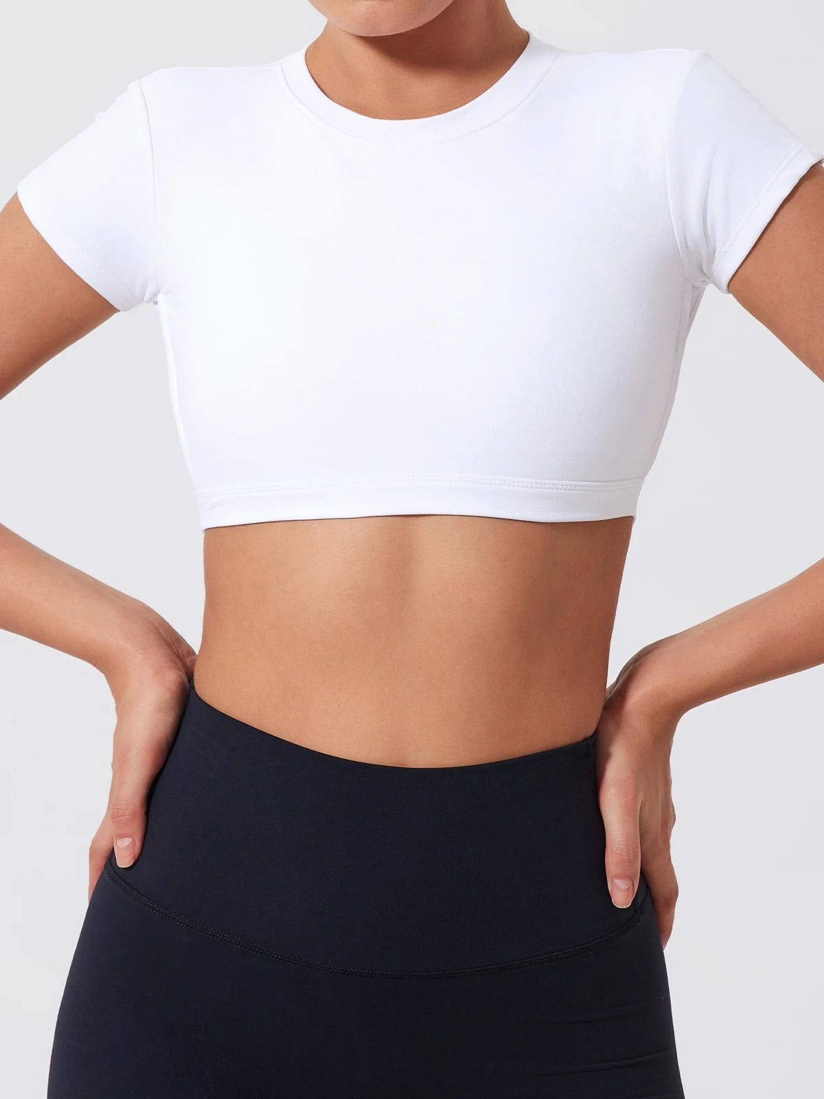 Person wearing a white crop top and black leggings on a plain background