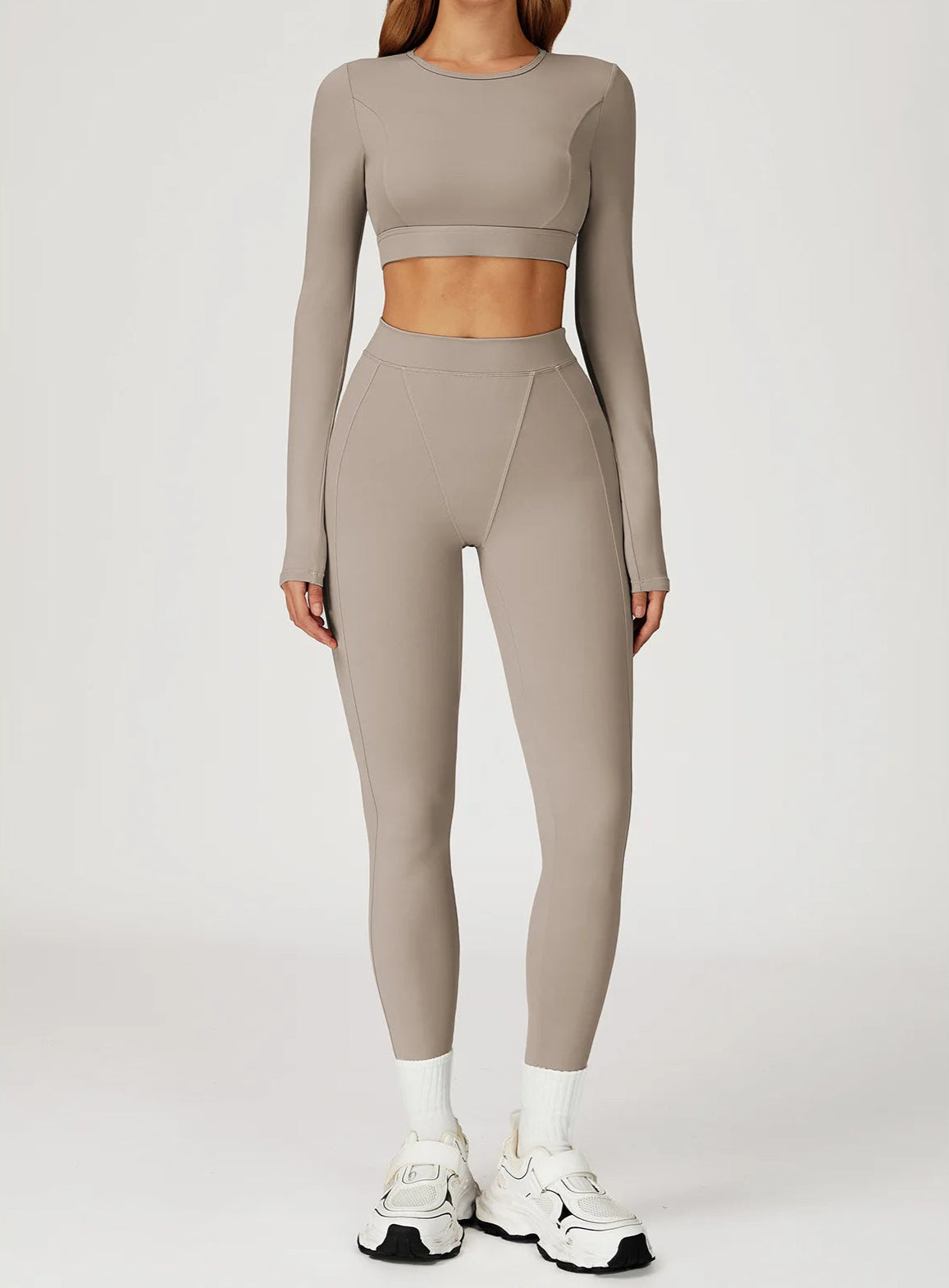 Person wearing a beige long-sleeve crop top and leggings set on a white background