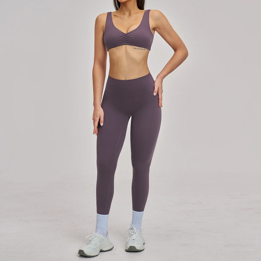 Person wearing a purple sports bra and leggings set on a plain background