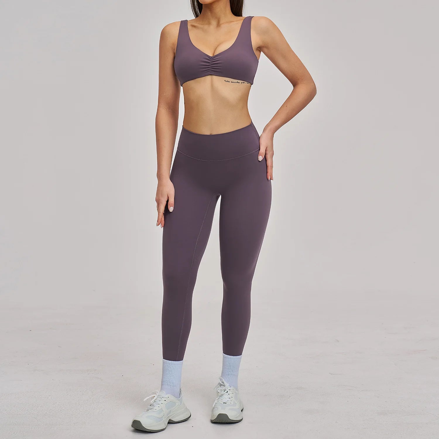 Person wearing a purple sports bra and leggings set on a plain background