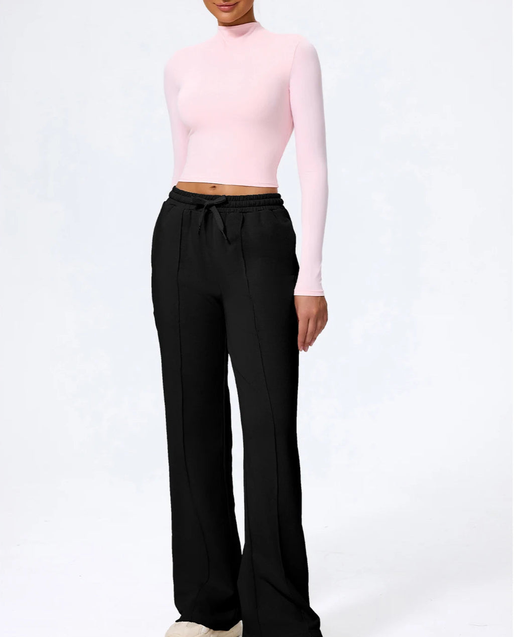 Person wearing a pink long-sleeve top and black wide-leg pants on a white background
