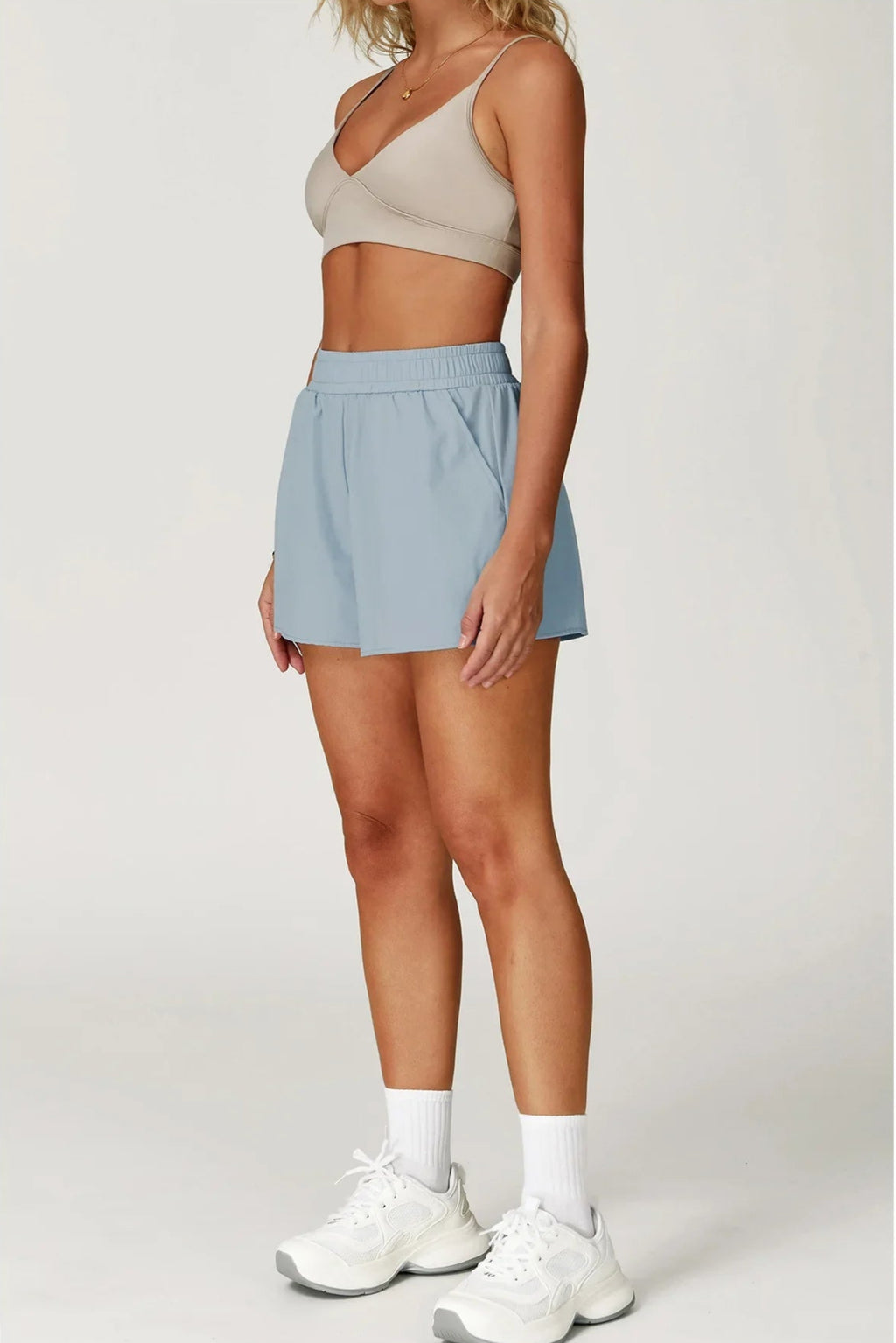 Person wearing a beige sports bra and light blue shorts on a white background