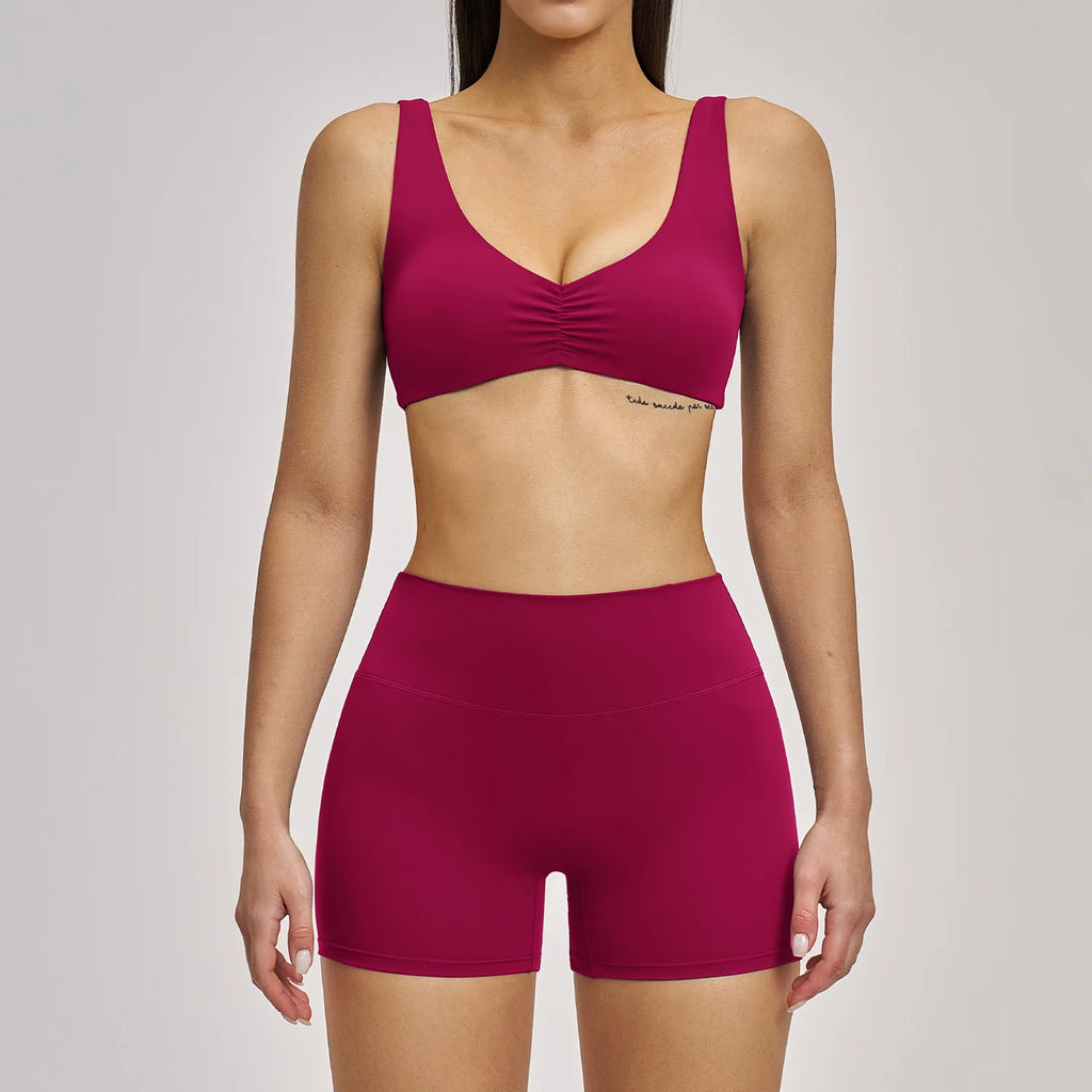 Person wearing a maroon sports bra and shorts set on a plain background