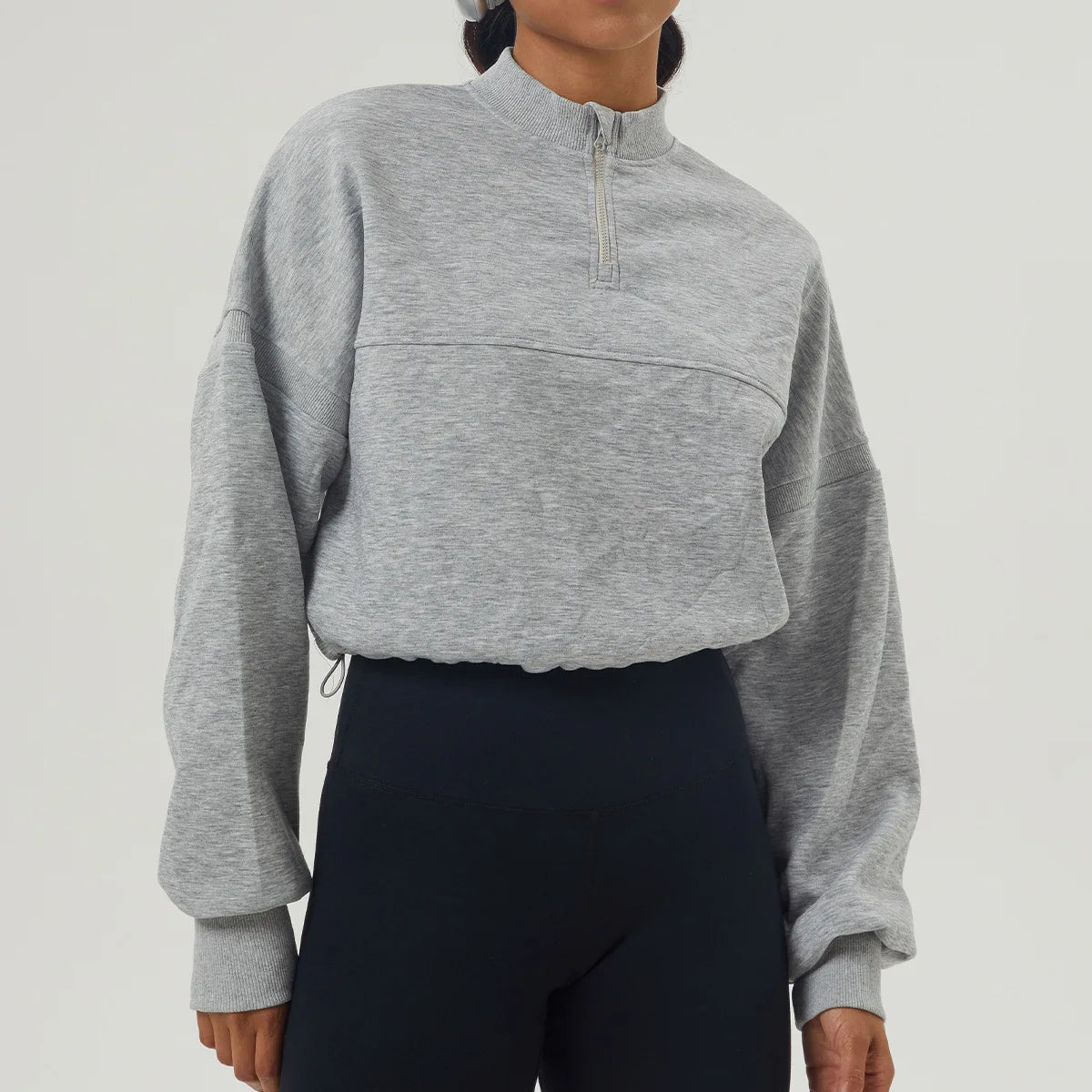 Person wearing a gray cropped sweatshirt with a zipper on a light gray background