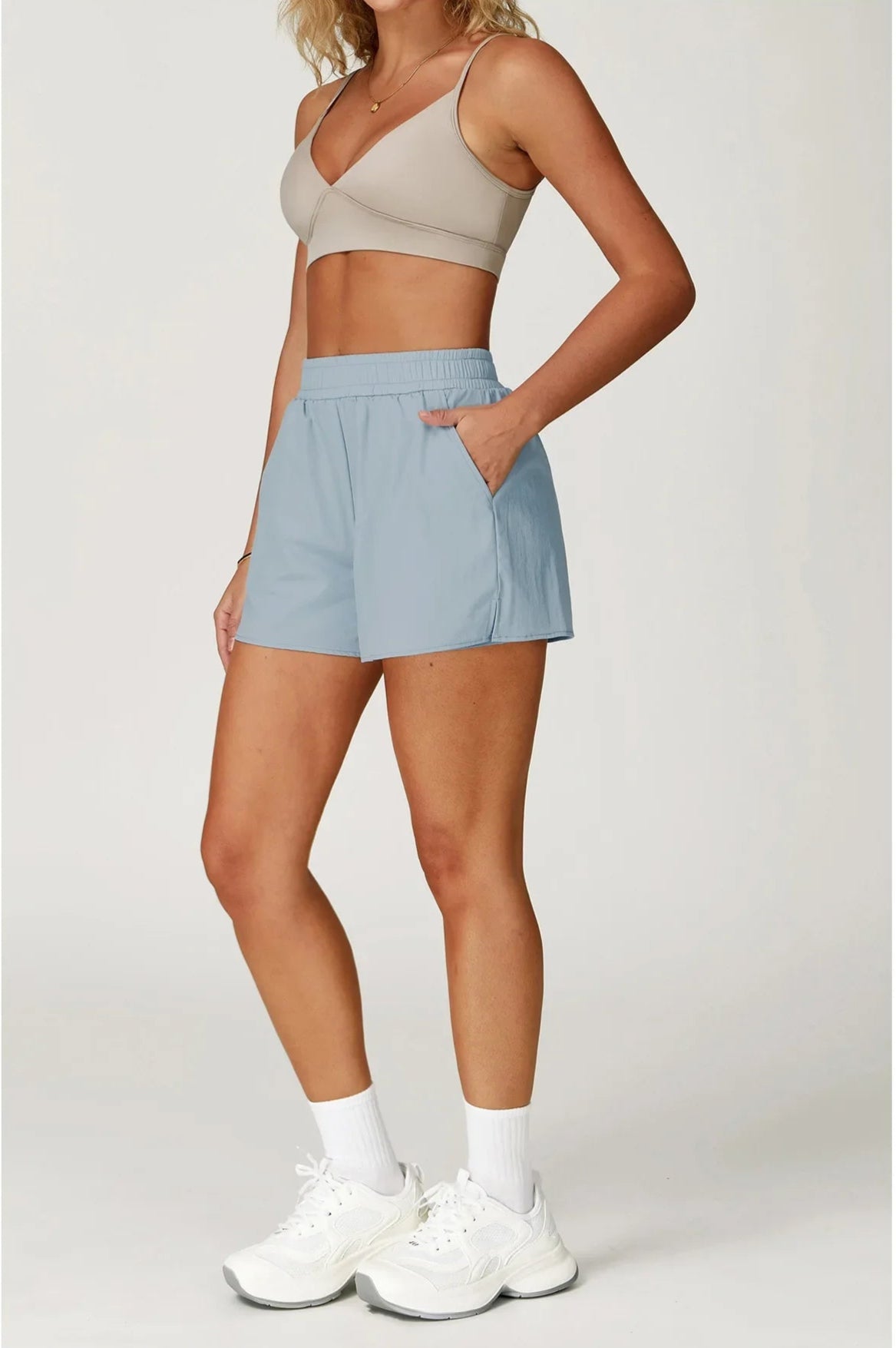 Woman wearing a beige sports bra and light blue shorts on a white background