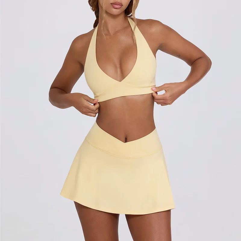 Woman wearing a lemon yellow sports bra and tennis skirt set on a plain background