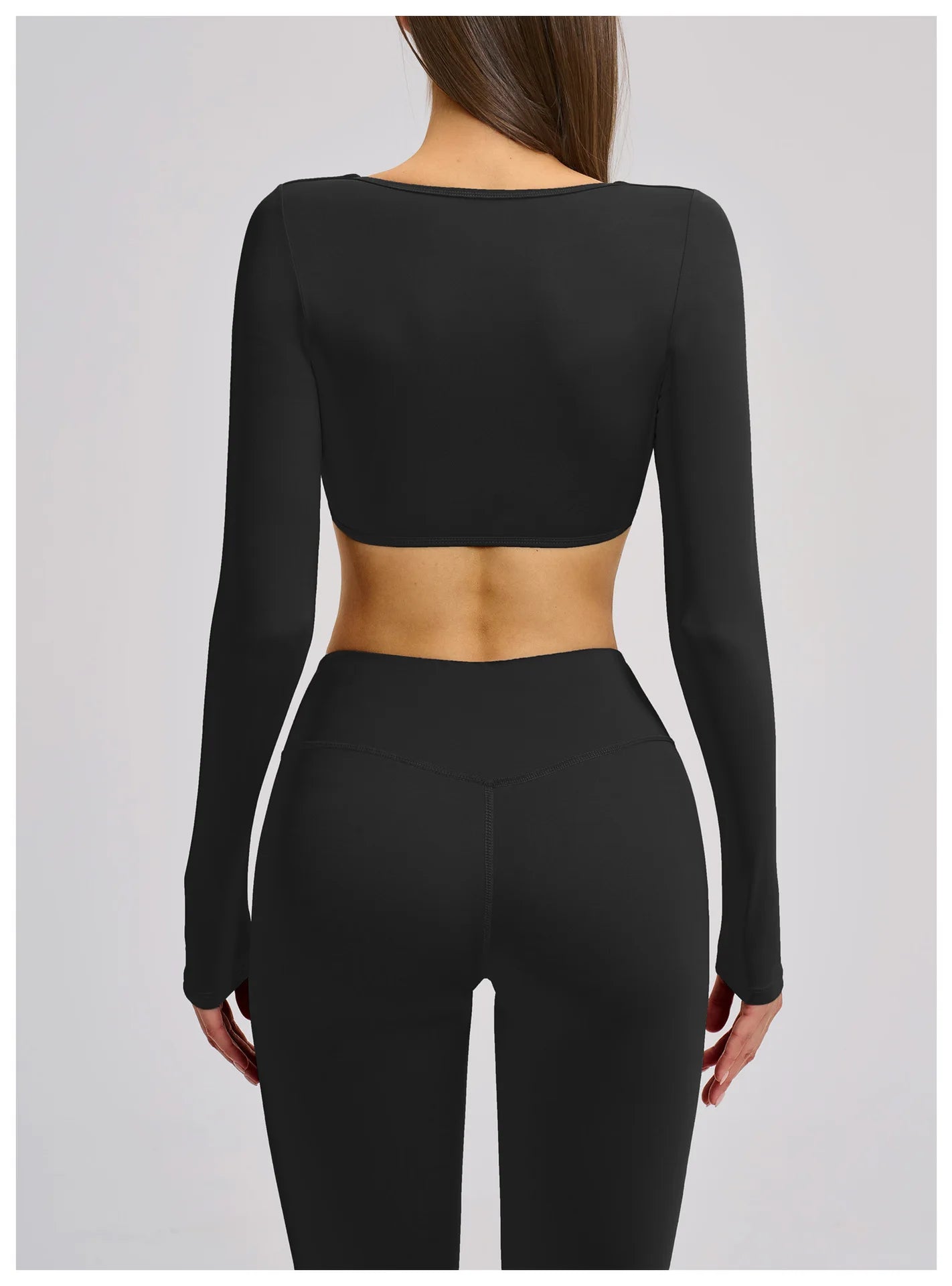 Person wearing a black long-sleeve crop top and leggings on a light gray background
