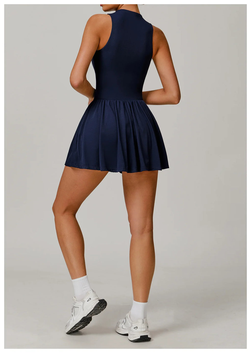 Person wearing a navy blue dress with white sneakers on a light gray background