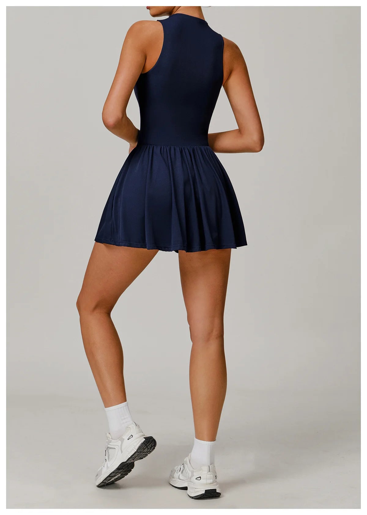 Person wearing a navy blue dress with white sneakers on a light gray background