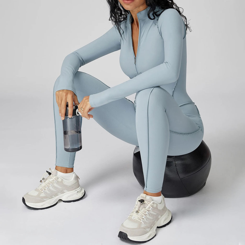 Person in a light blue athletic jumpsuit sitting on a black exercise ball with a white background