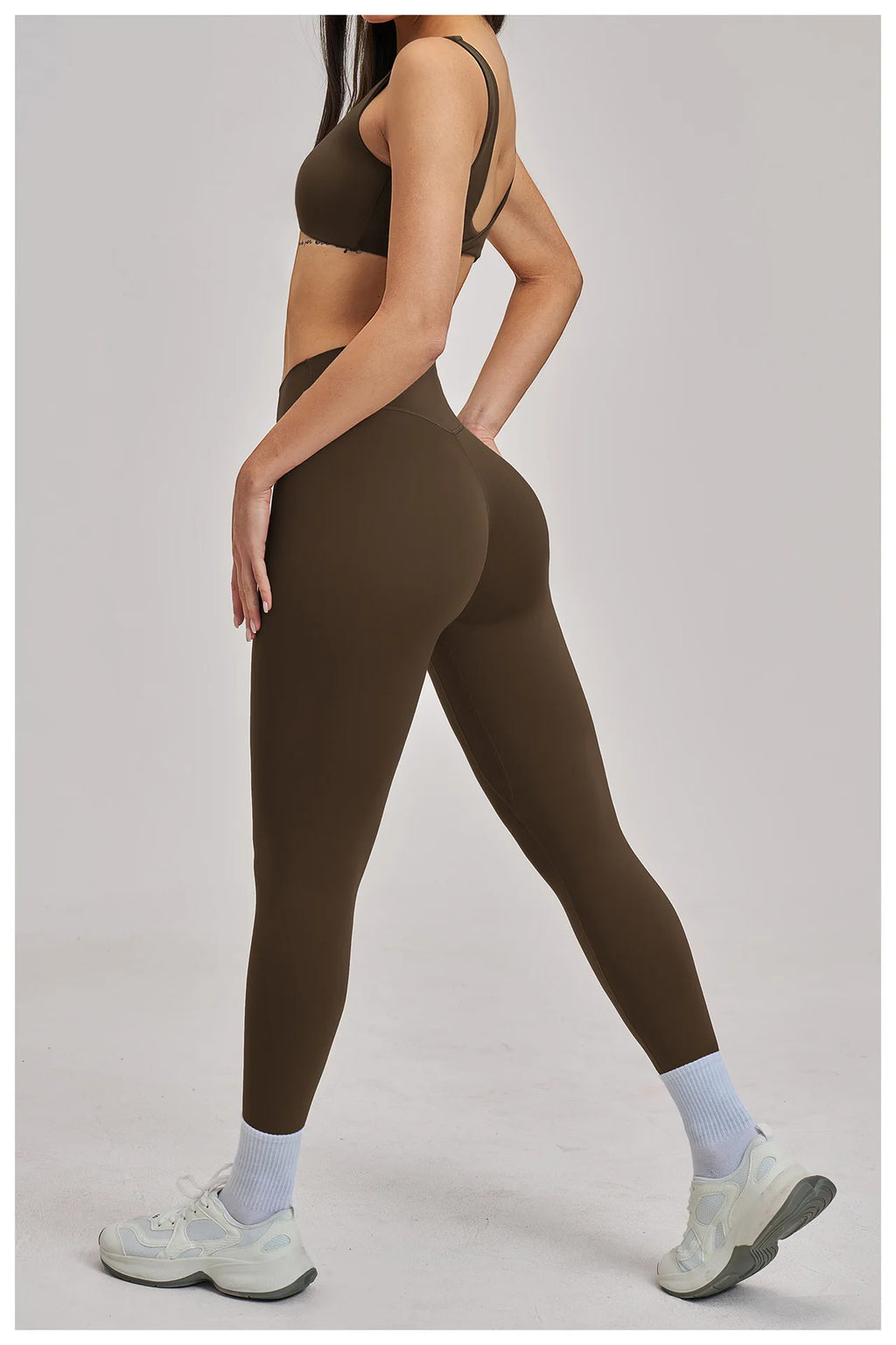 Person wearing brown athletic leggings and sports bra on a light gray background