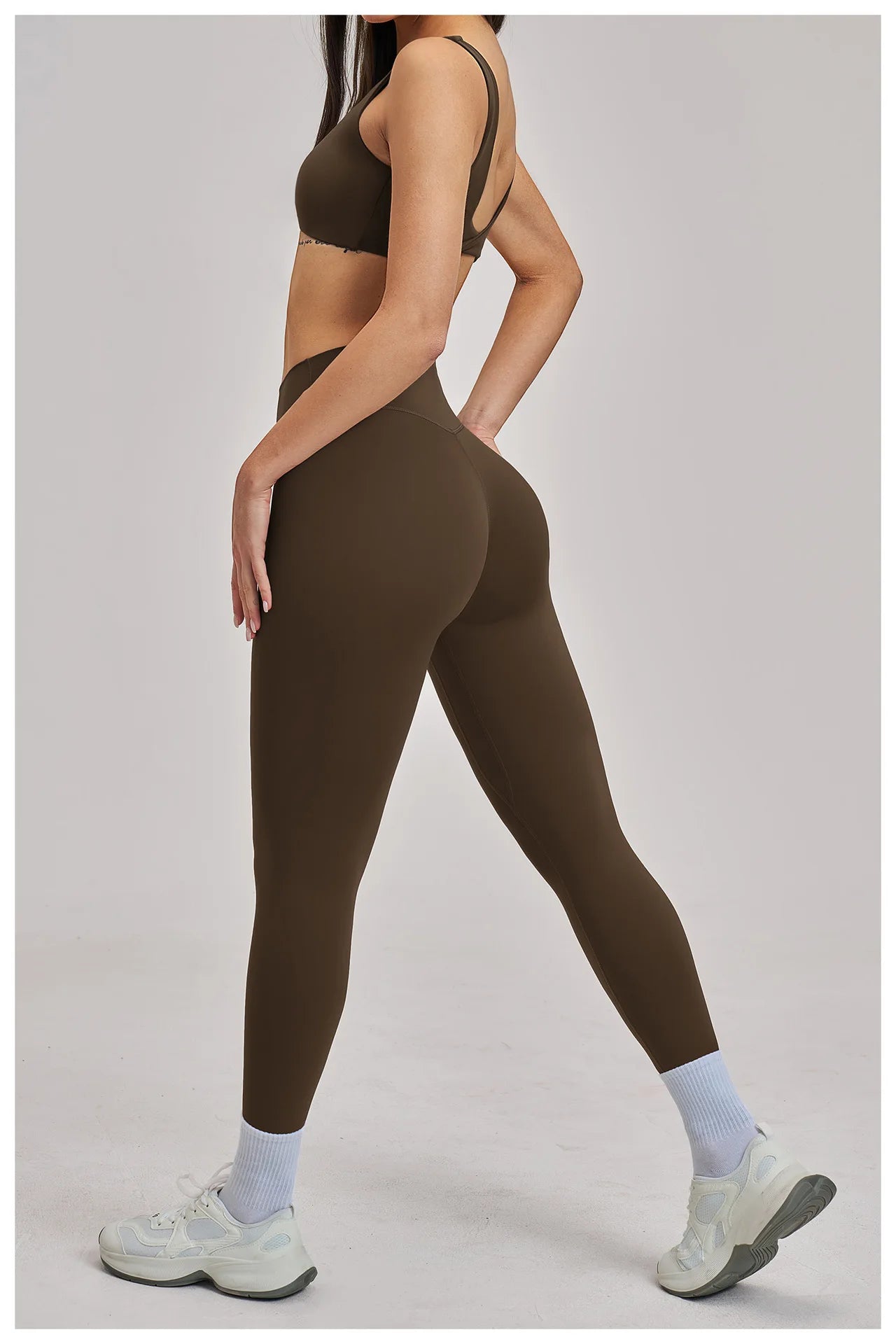 Person wearing brown athletic leggings and sports bra on a light gray background