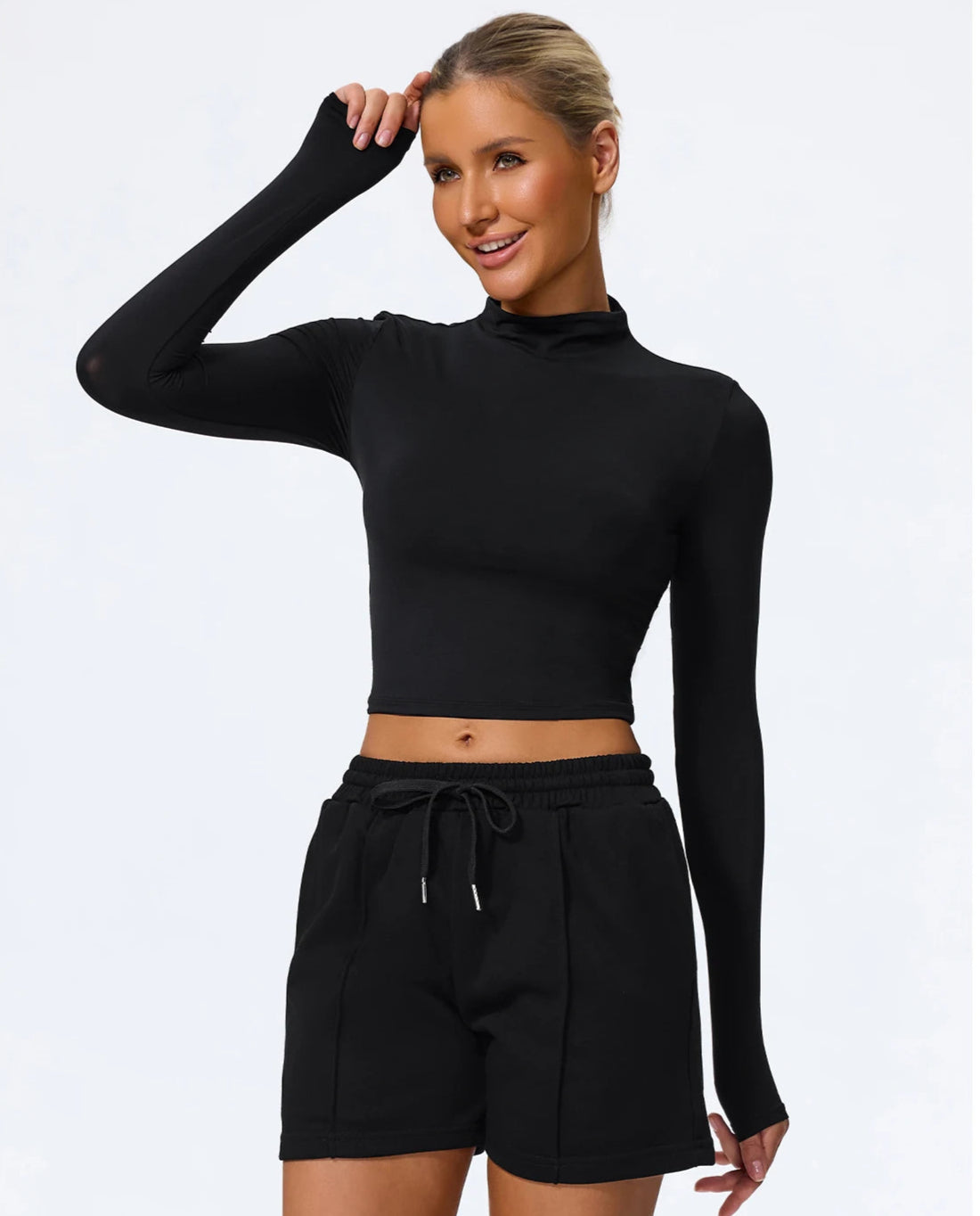Woman wearing a black long-sleeve crop top and black shorts on a white background