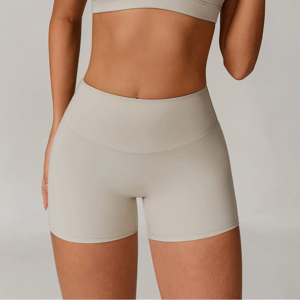 Woman wearing a beige sports bra and shorts set against a plain background