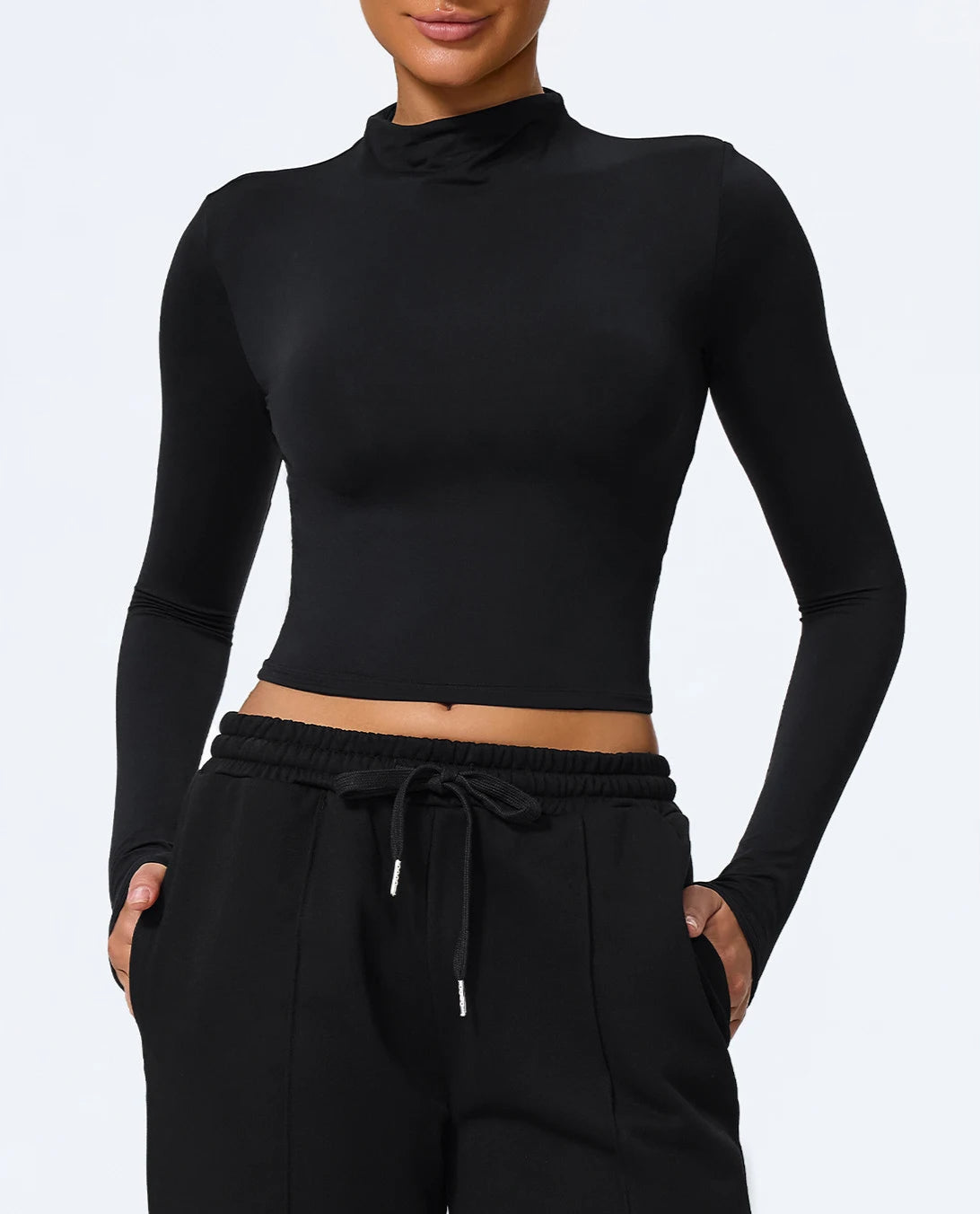 Person wearing a black long-sleeve crop top and black drawstring pants on a white background