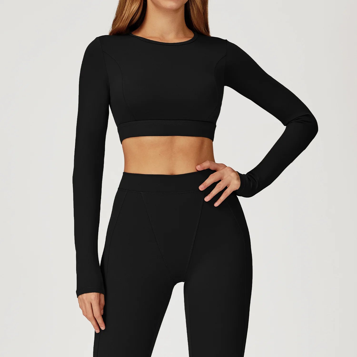 Person wearing a black long-sleeve crop top and leggings on a light gray background