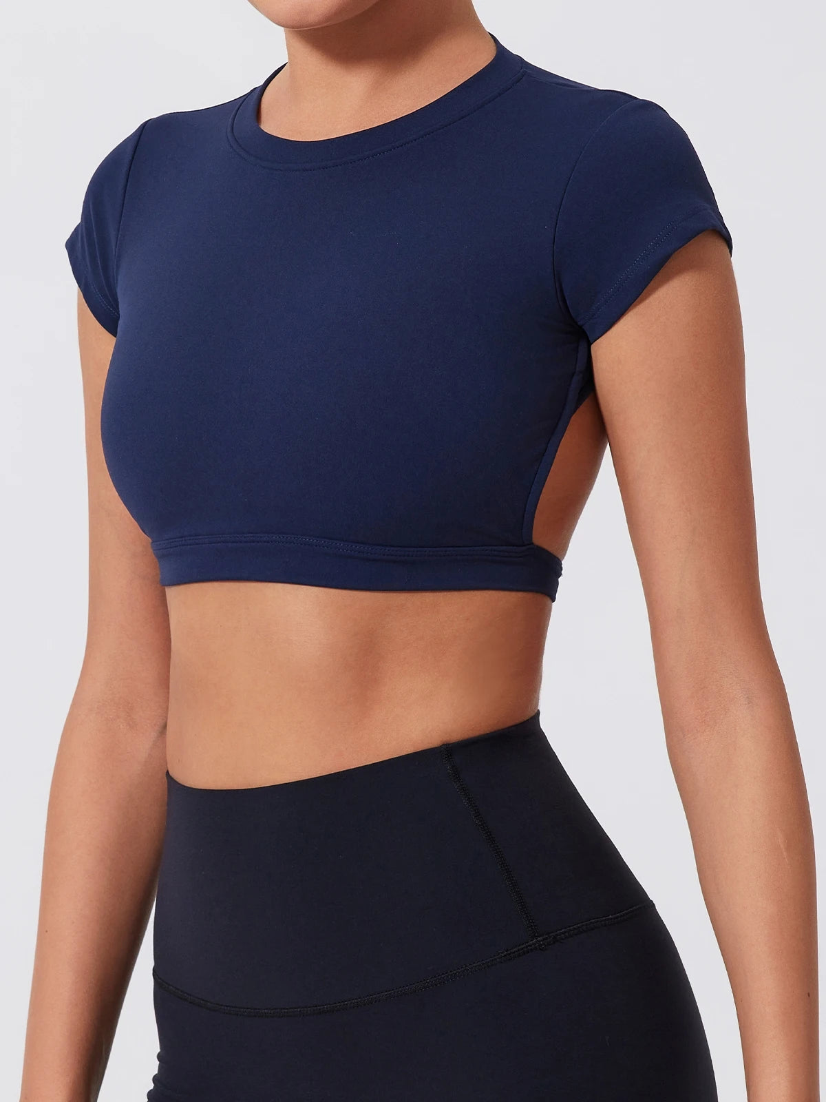 Person wearing a navy blue athletic crop top and leggings on a light gray background