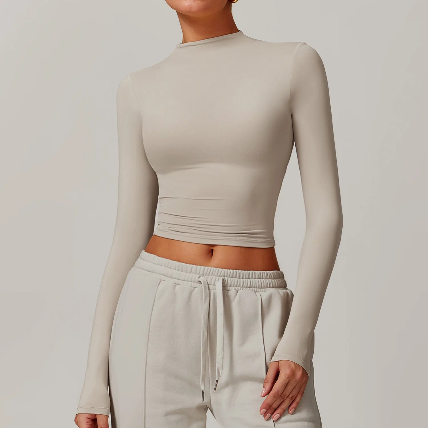 Person wearing a beige long-sleeve crop top and matching pants against a plain background