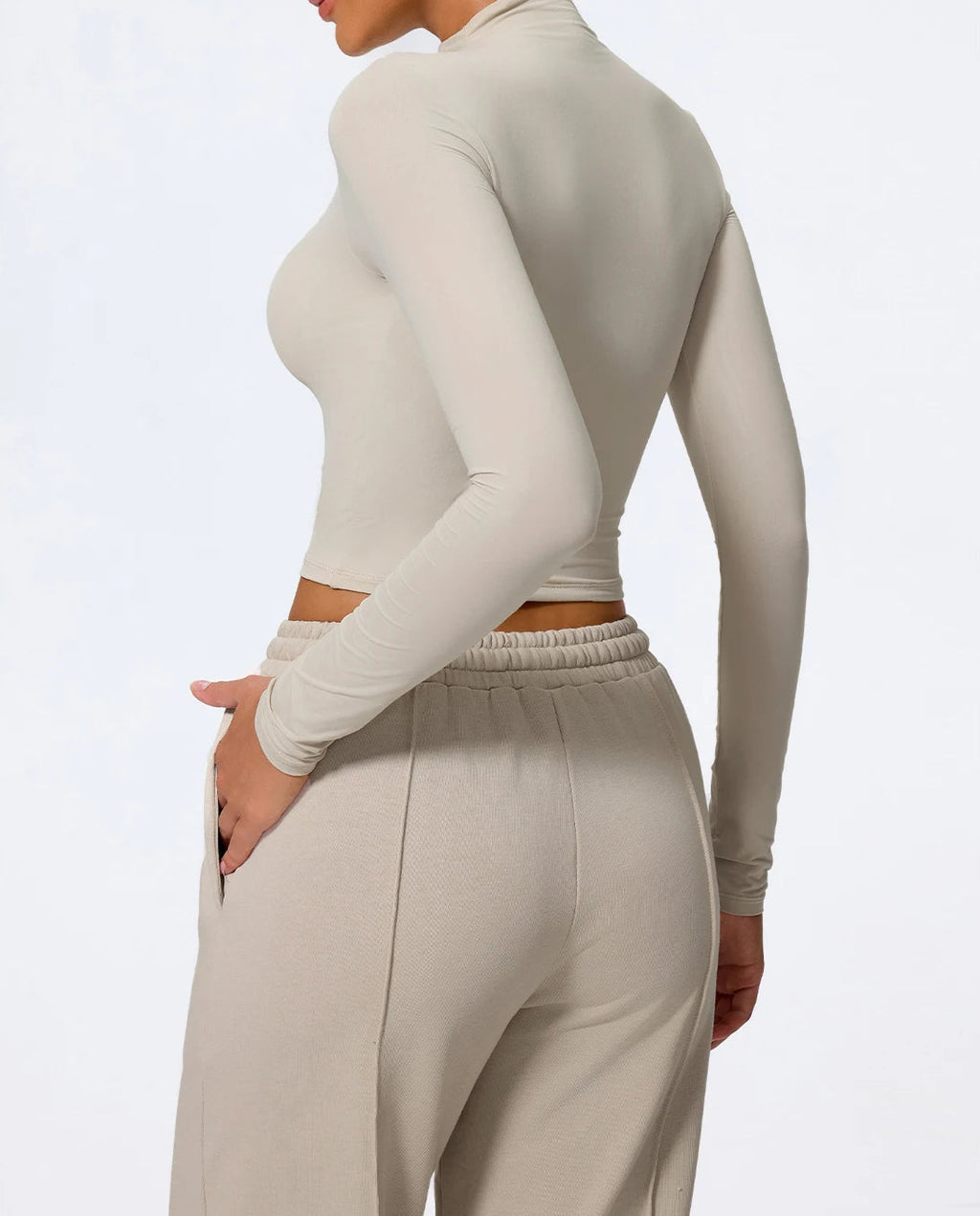Person wearing a beige long-sleeve top and matching pants on a light gray background