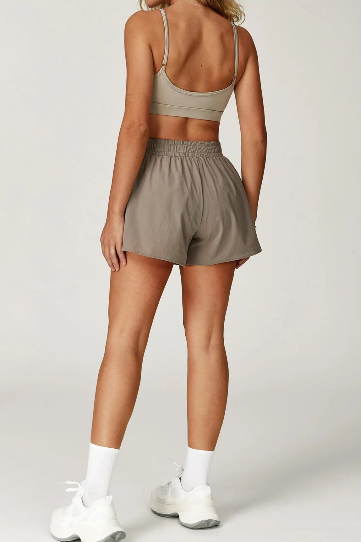Person wearing a beige sports bra and shorts set on a plain background