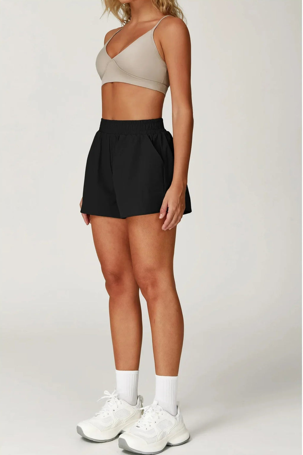 Person wearing a beige sports bra and black shorts on a white background