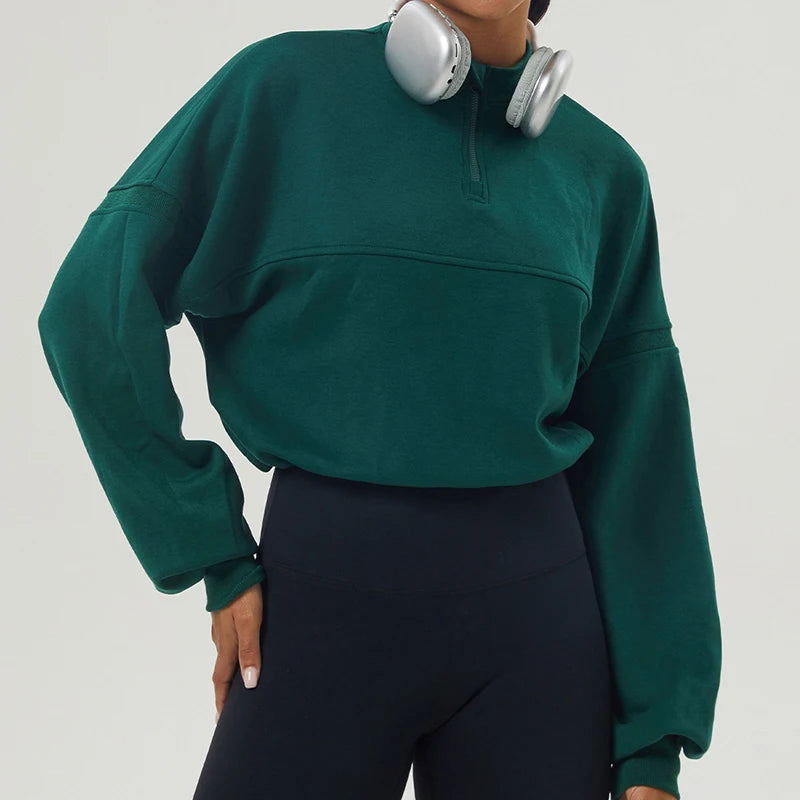 Person wearing a green sweatshirt and black pants with silver headphones on a light gray background