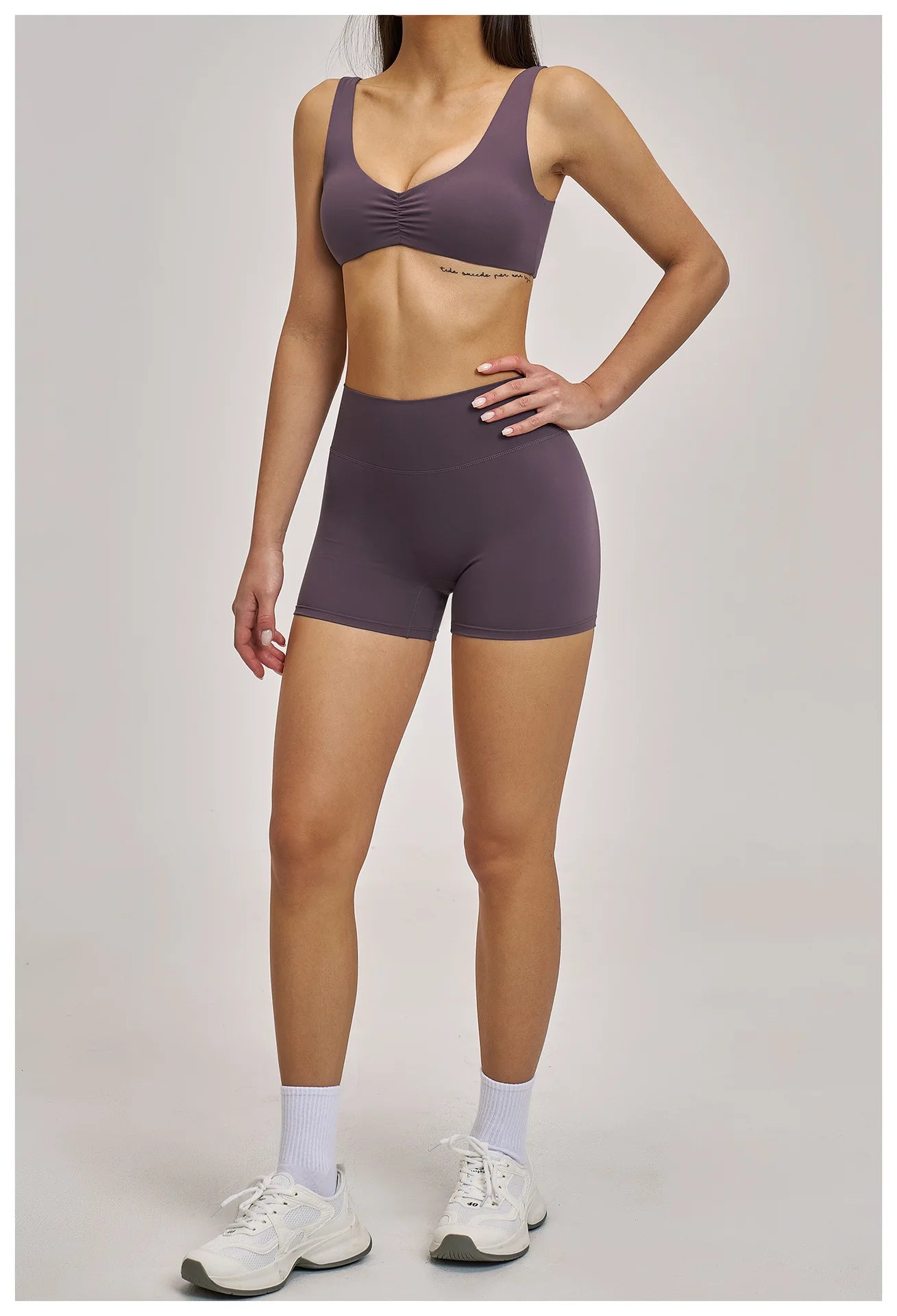 Person wearing a matching purple sports bra and high-waisted shorts on a plain background