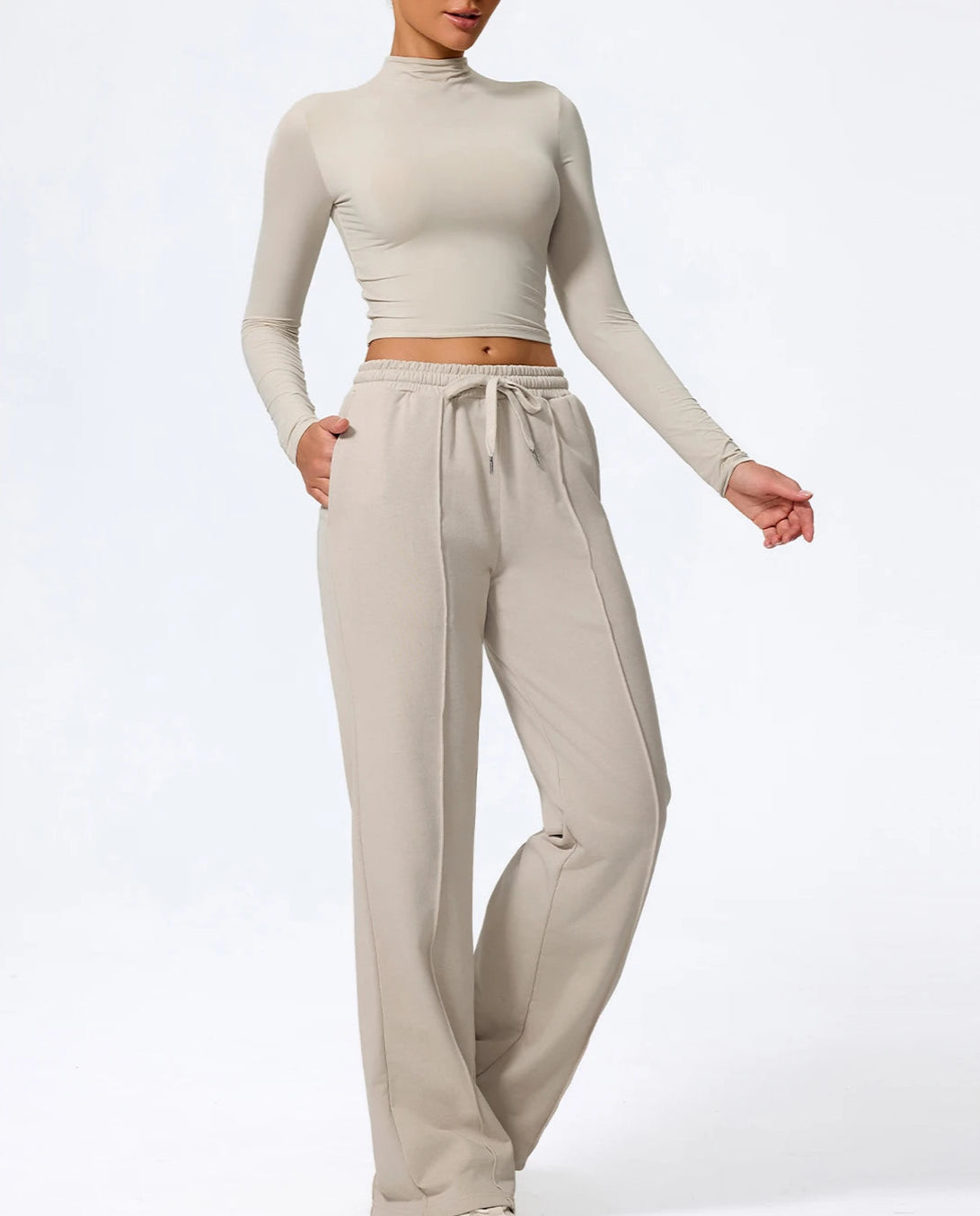 Person wearing a beige long-sleeve top and wide-leg pants on a white background