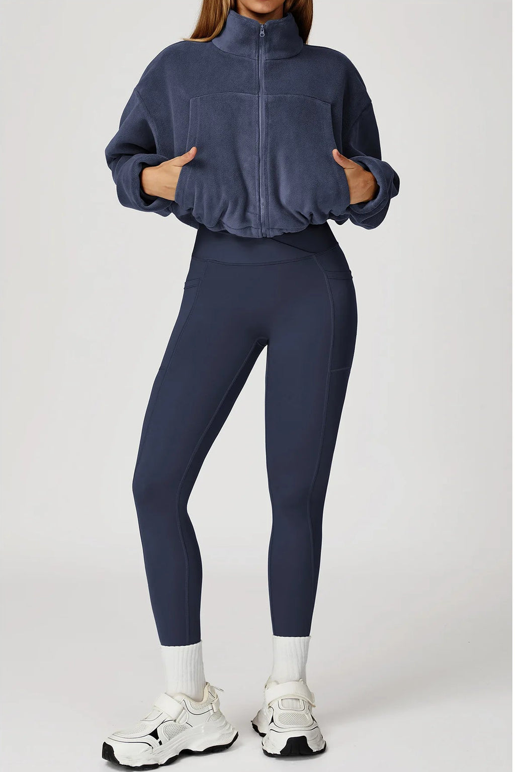 Person wearing a navy tracksuit with white sneakers on a light gray background