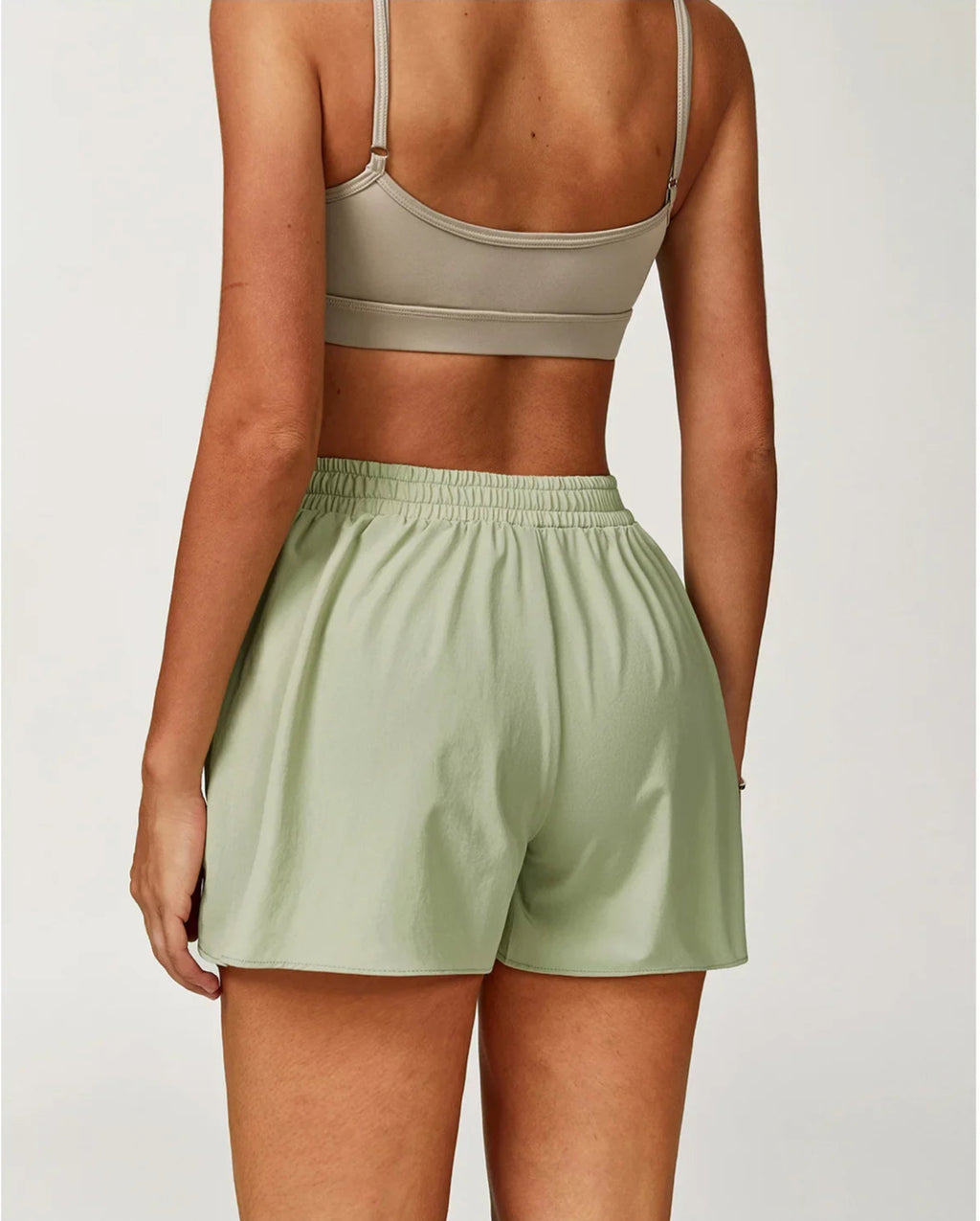 Person wearing a beige sports bra and green shorts on a plain background