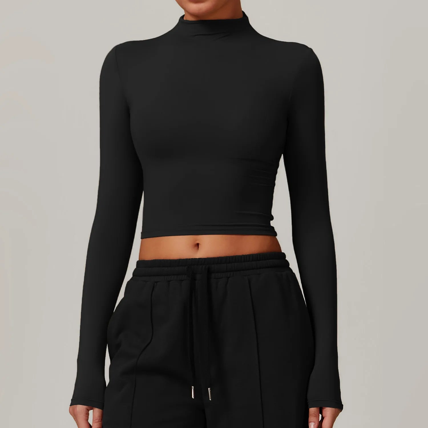 Person wearing a black long-sleeve crop top and black pants on a gray background