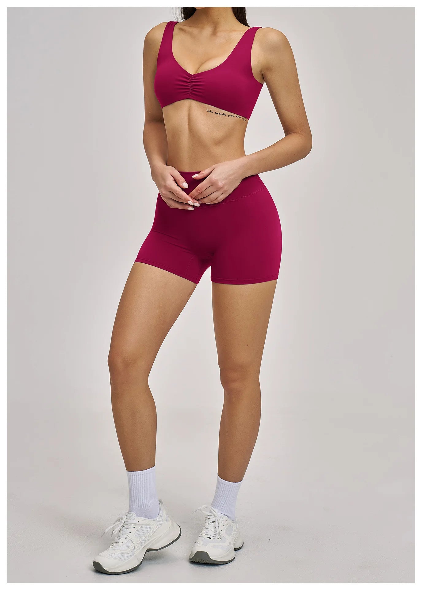 Person wearing a maroon sports bra and shorts set on a plain background