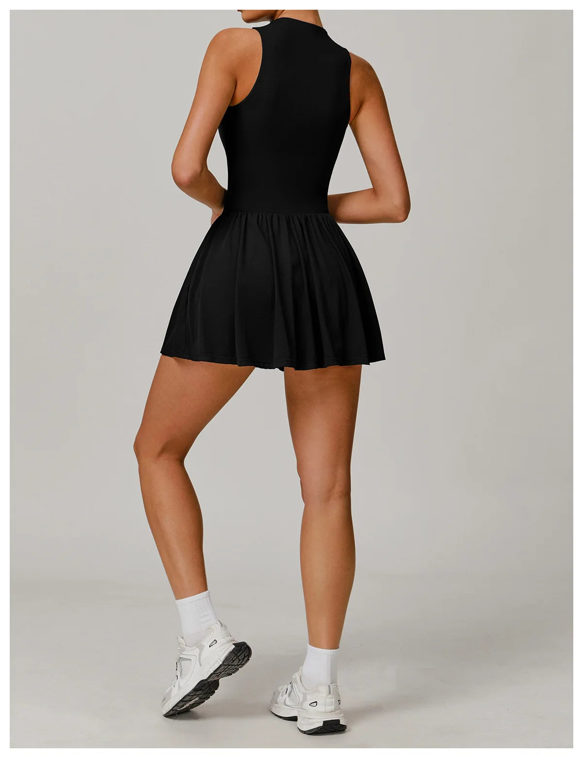 Person wearing a black dress with white sneakers on a plain background