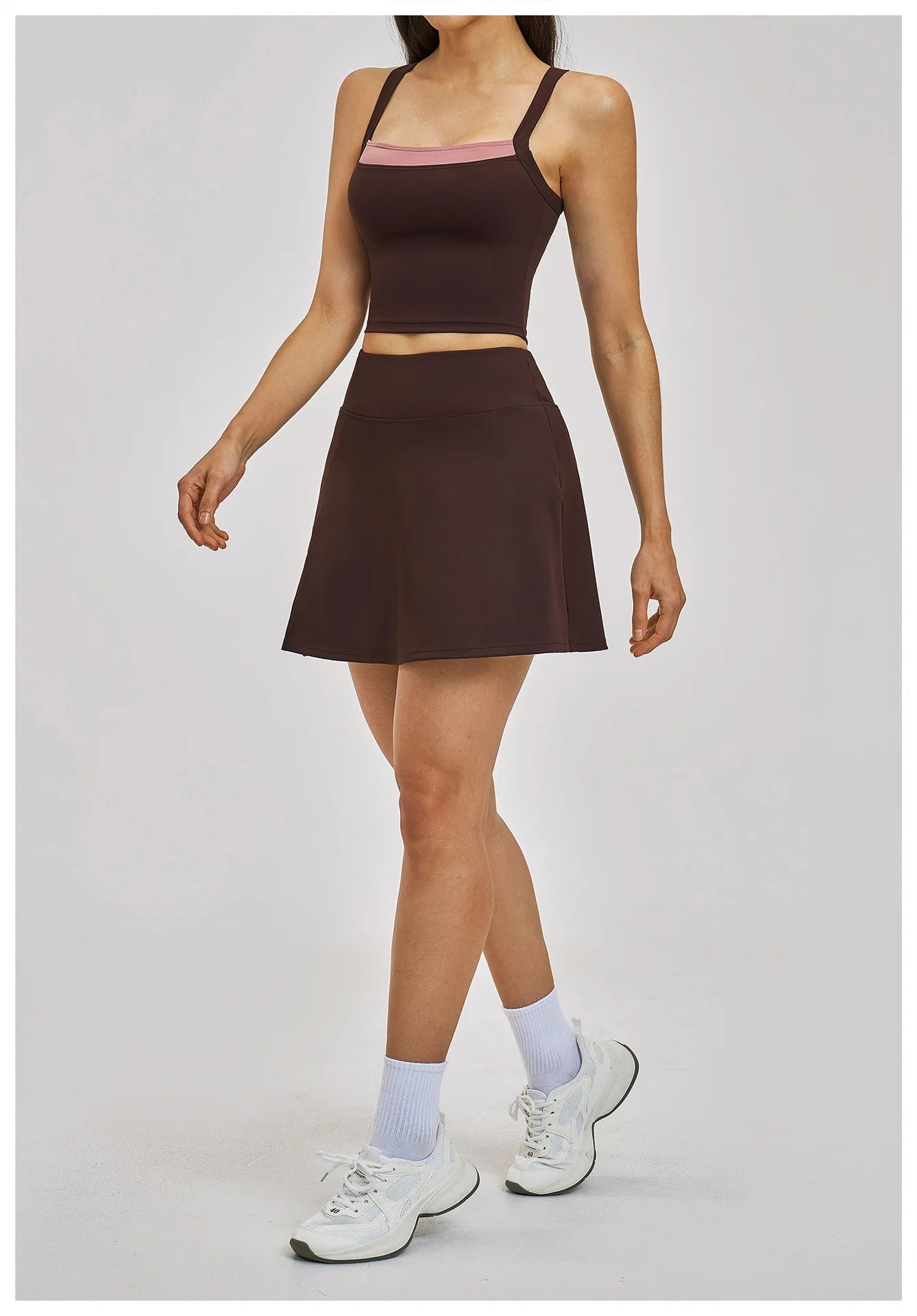 Person wearing a brown two-piece outfit with white sneakers and light purple socks on a gray background