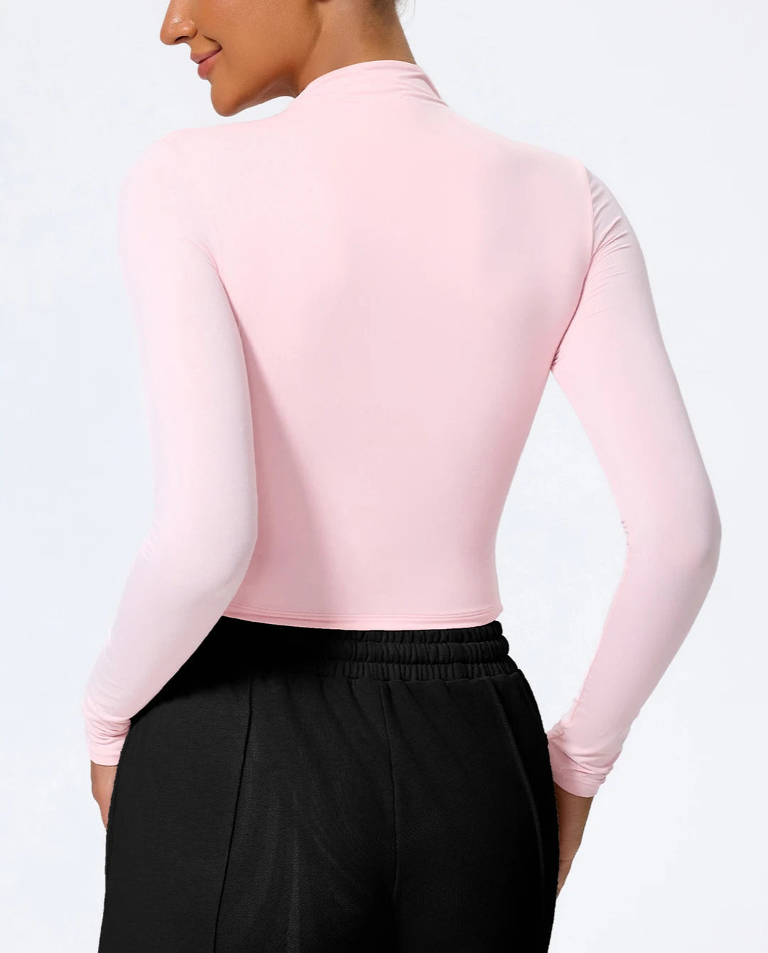 Person wearing a pink long-sleeve top and black pants on a white background