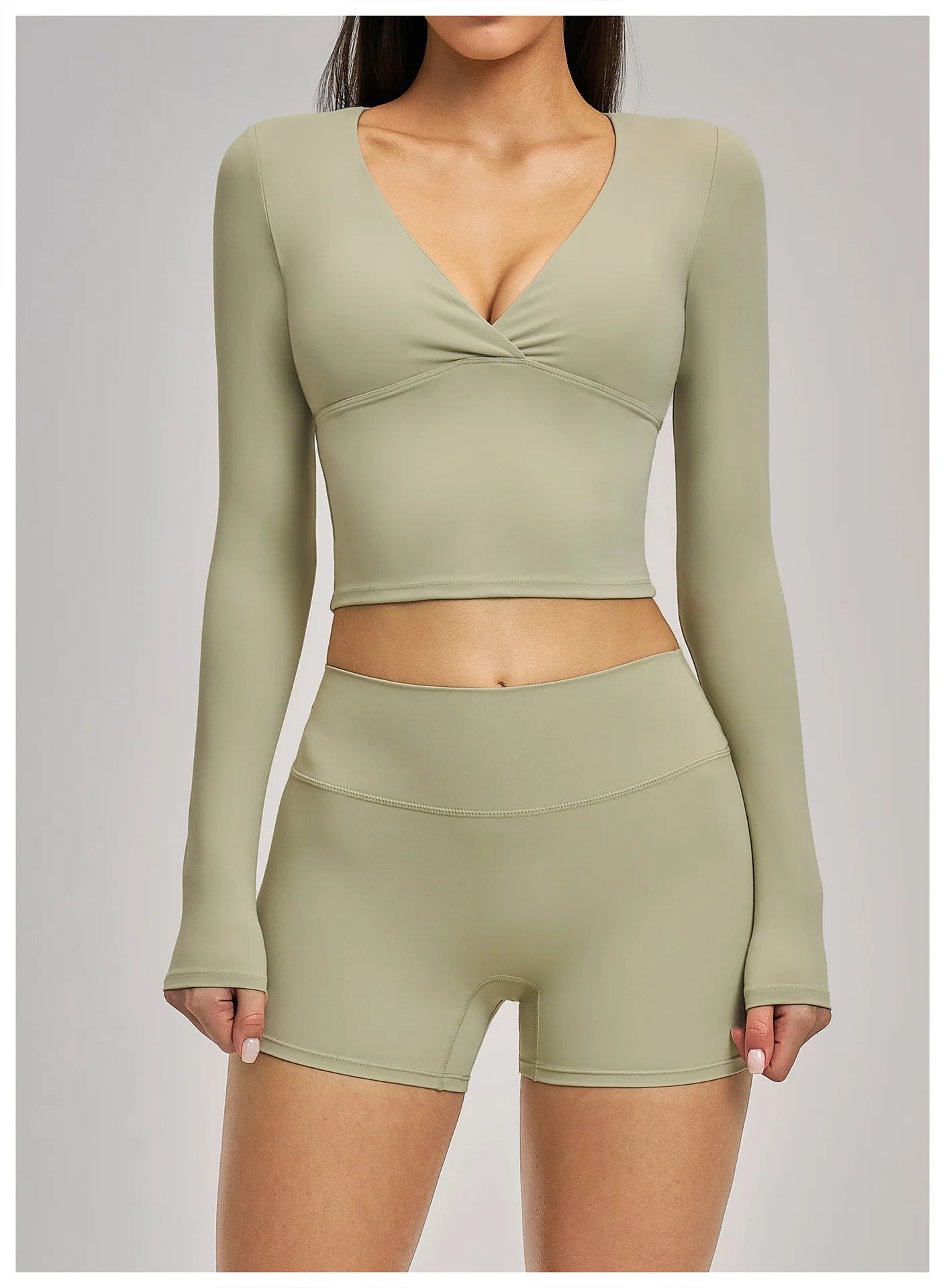 Person wearing a green long-sleeve crop top and shorts set on a plain background