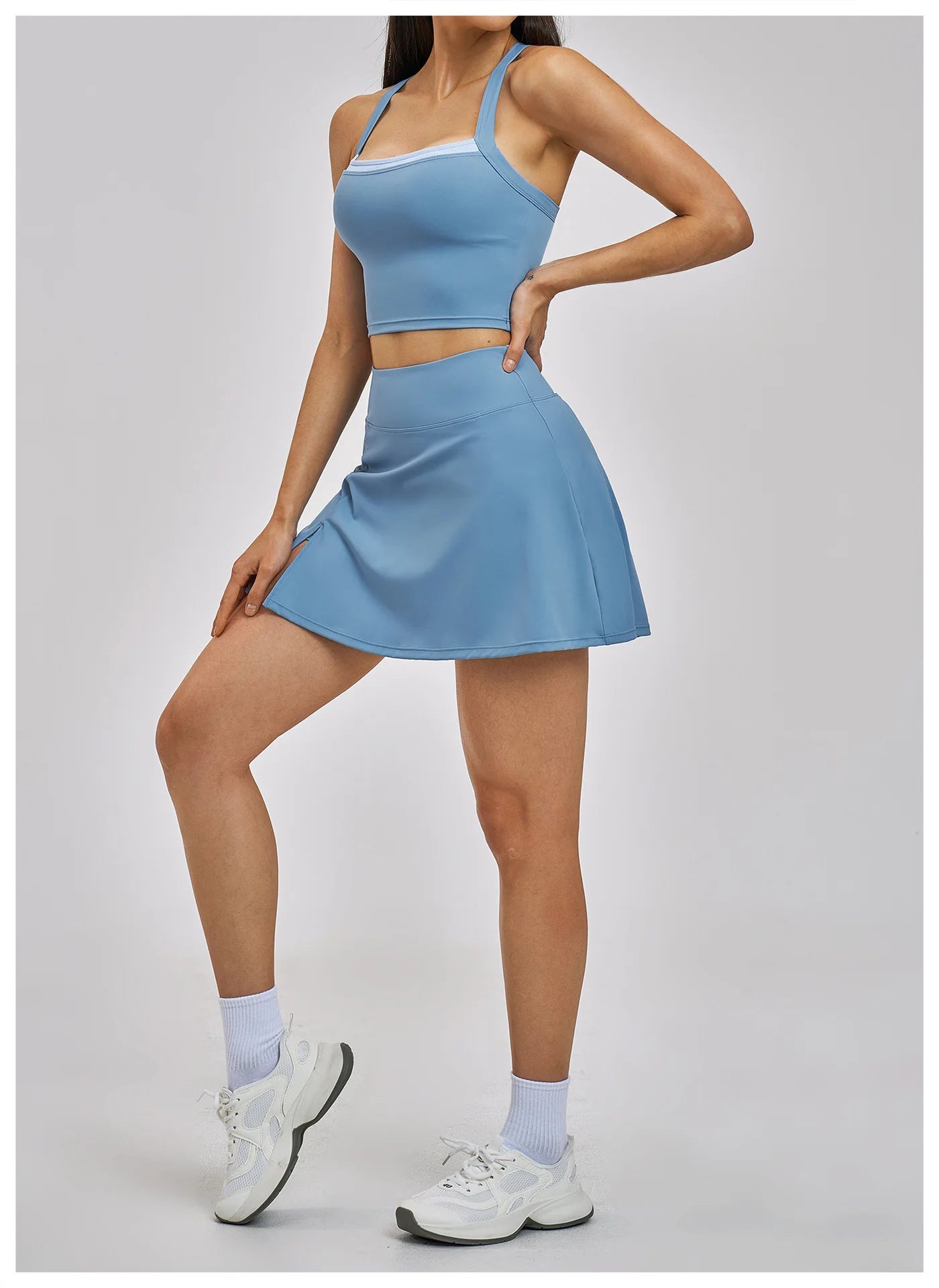Woman wearing a blue athletic outfit with a skirt on a plain background