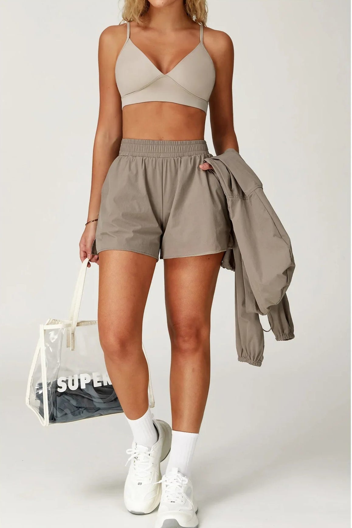 Woman wearing a beige sports bra and shorts with a matching jacket on a white background