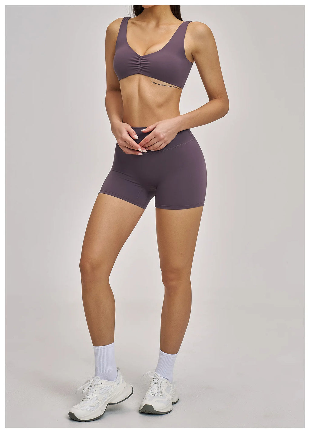 Person wearing a matching purple sports bra and shorts set on a plain background