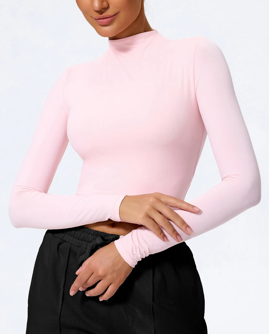 Person wearing a pink long-sleeve top and black pants on a white background