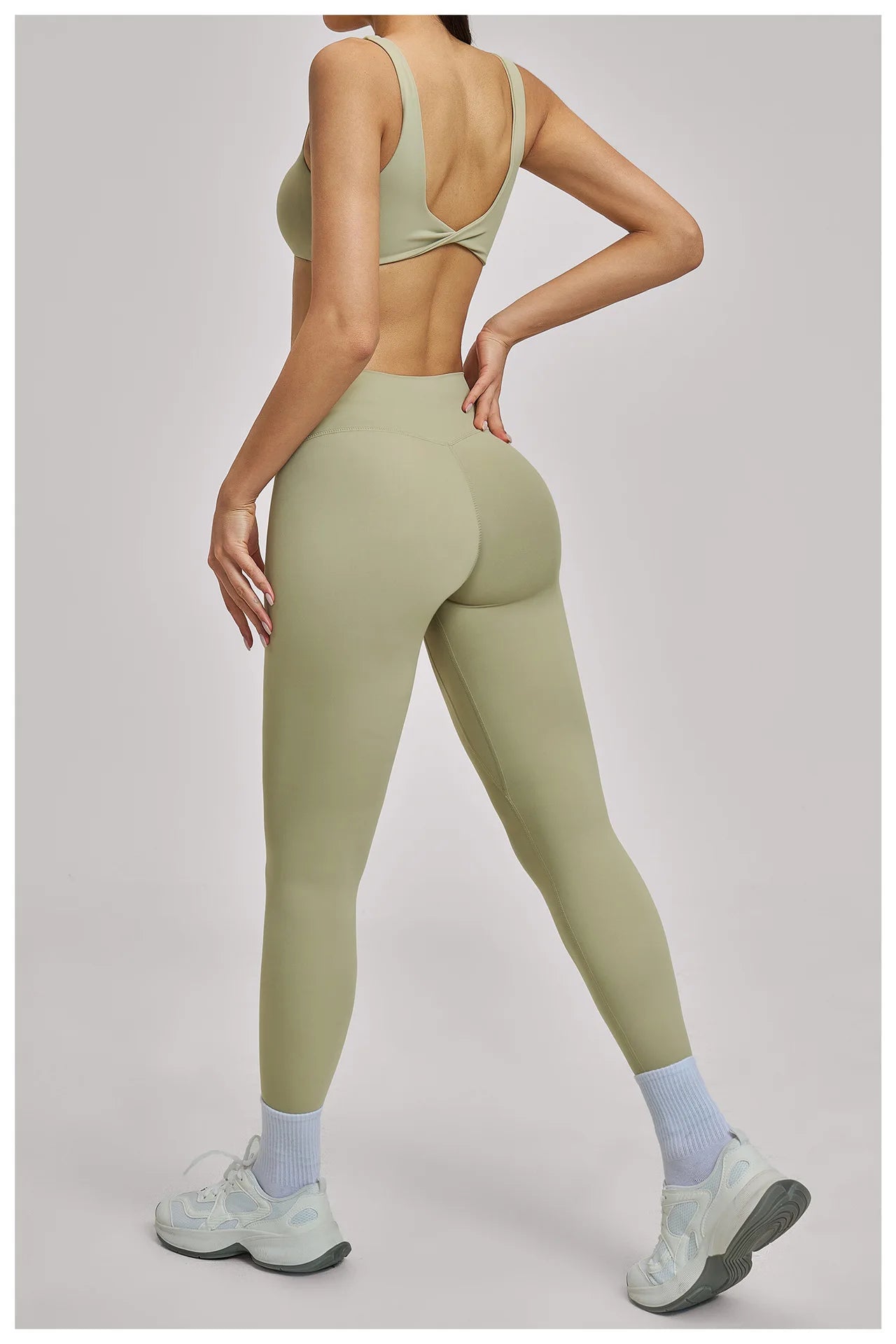 Person wearing olive green athletic leggings and sports bra on a plain background