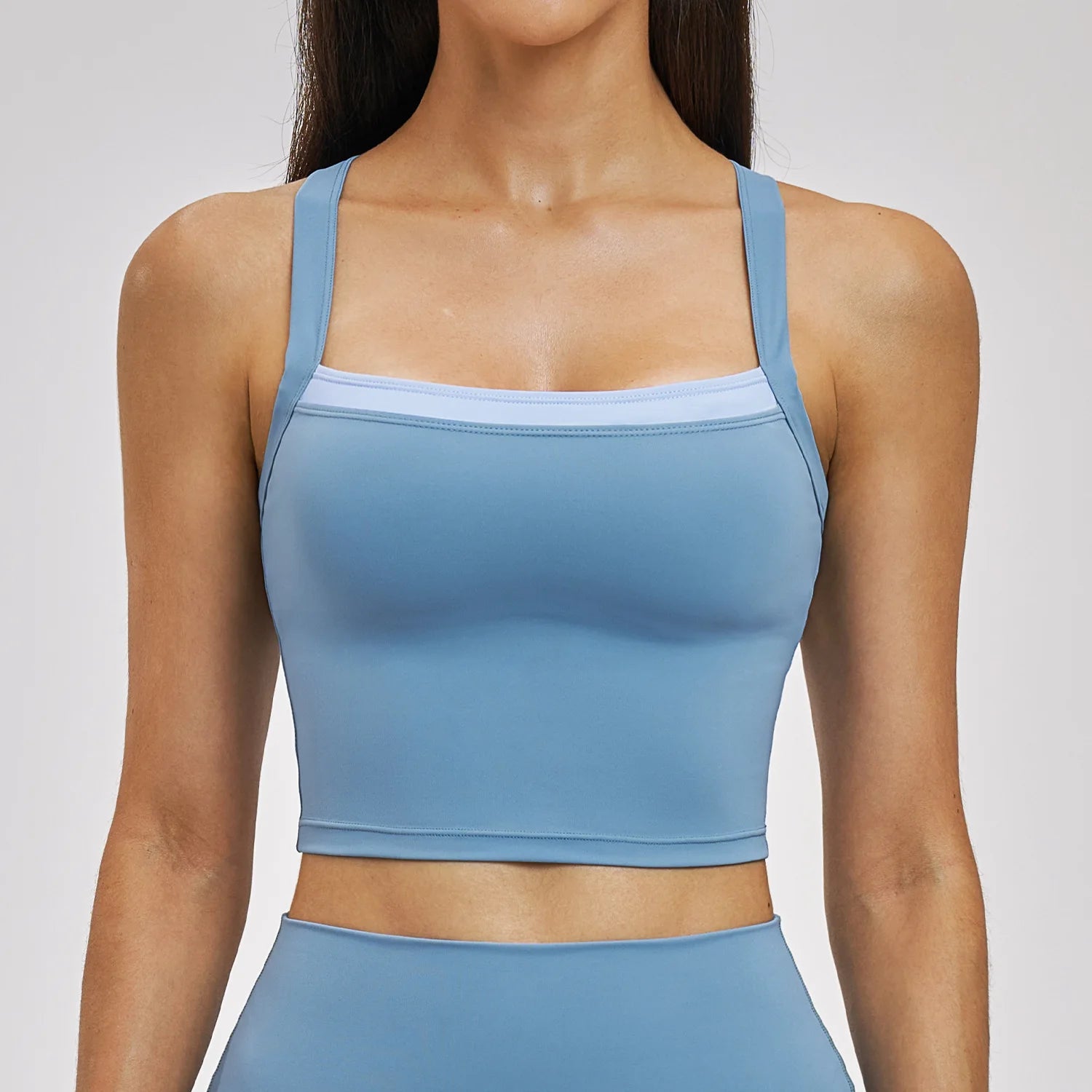 Woman wearing a blue sports bra and leggings on a light gray background