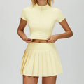 Woman wearing a butter yellow outfit with a top and pleated tennis skirt on a white background