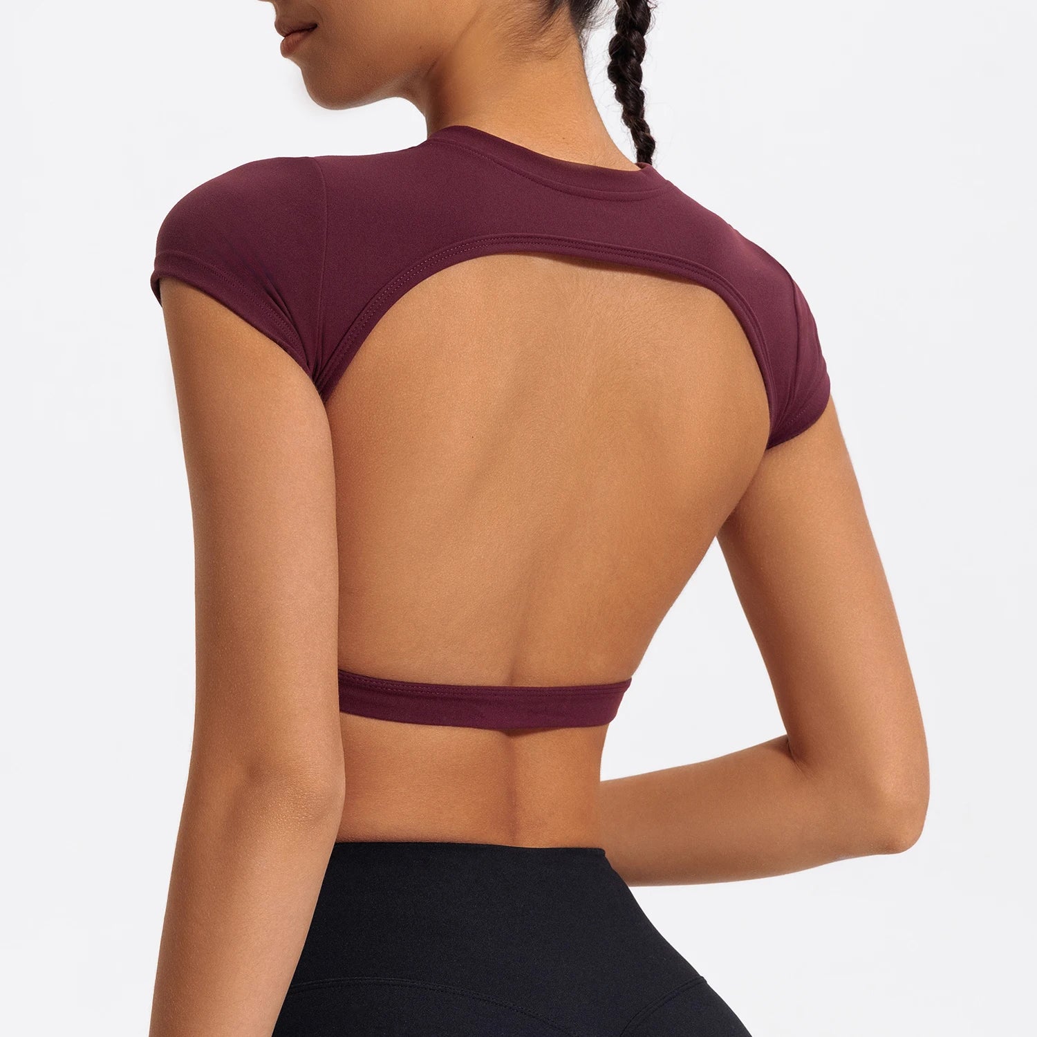 Woman wearing a maroon sports bra and black leggings on a light gray background