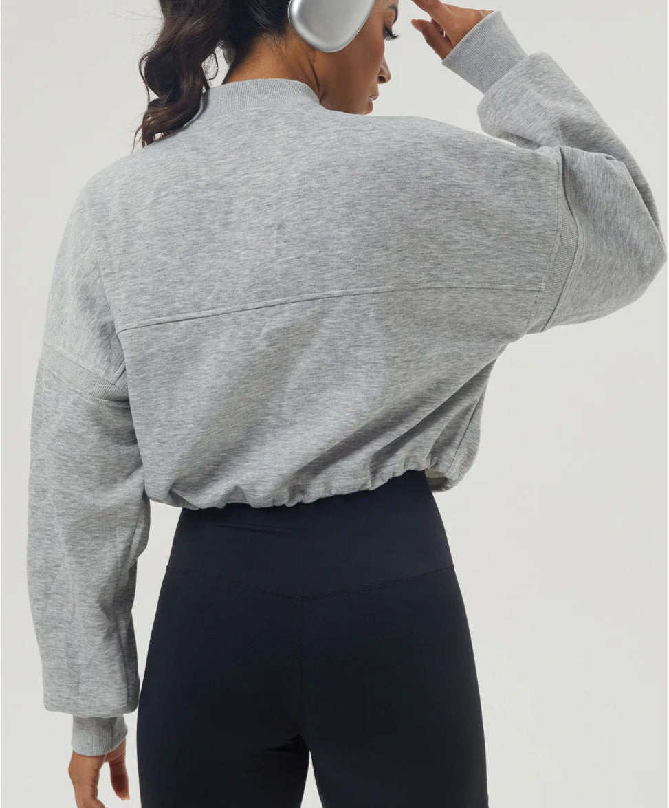 Person wearing a gray cropped sweatshirt and black leggings on a light gray background