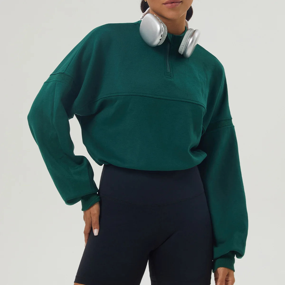 Person wearing a green sweatshirt and black pants with silver headphones on a white background