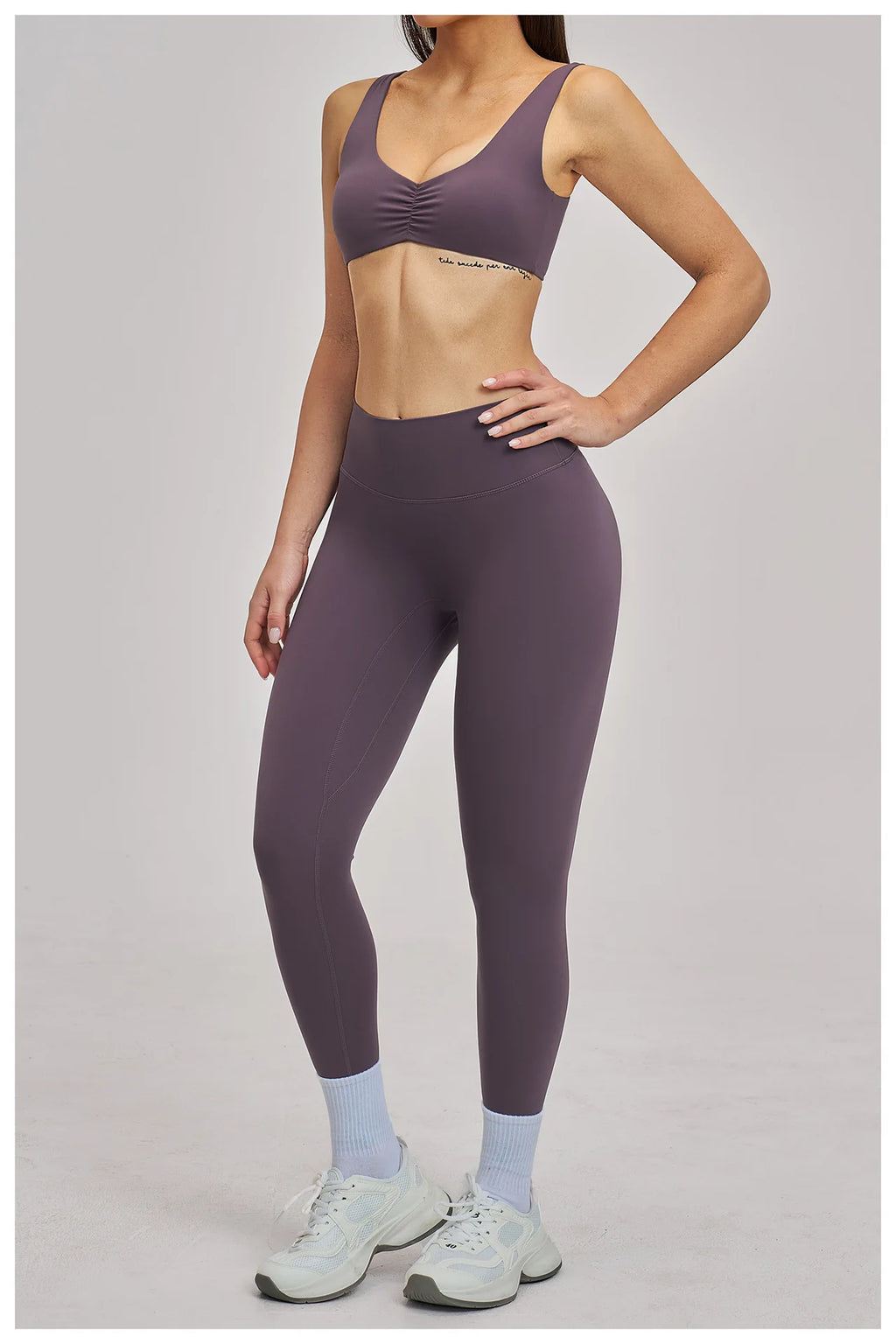 Person wearing a purple sports bra and leggings set on a plain background