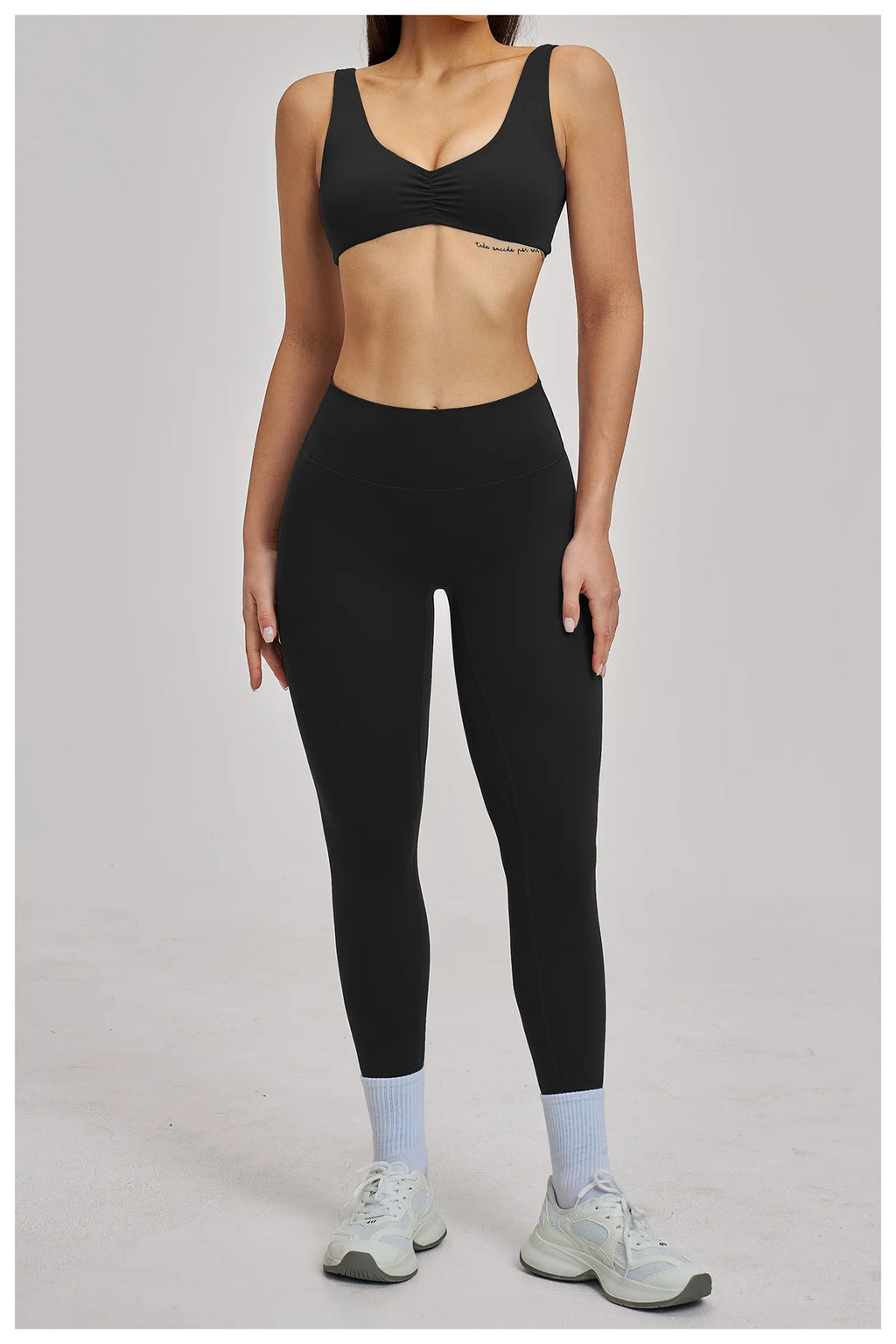 Person wearing a black sports bra and leggings set on a plain background