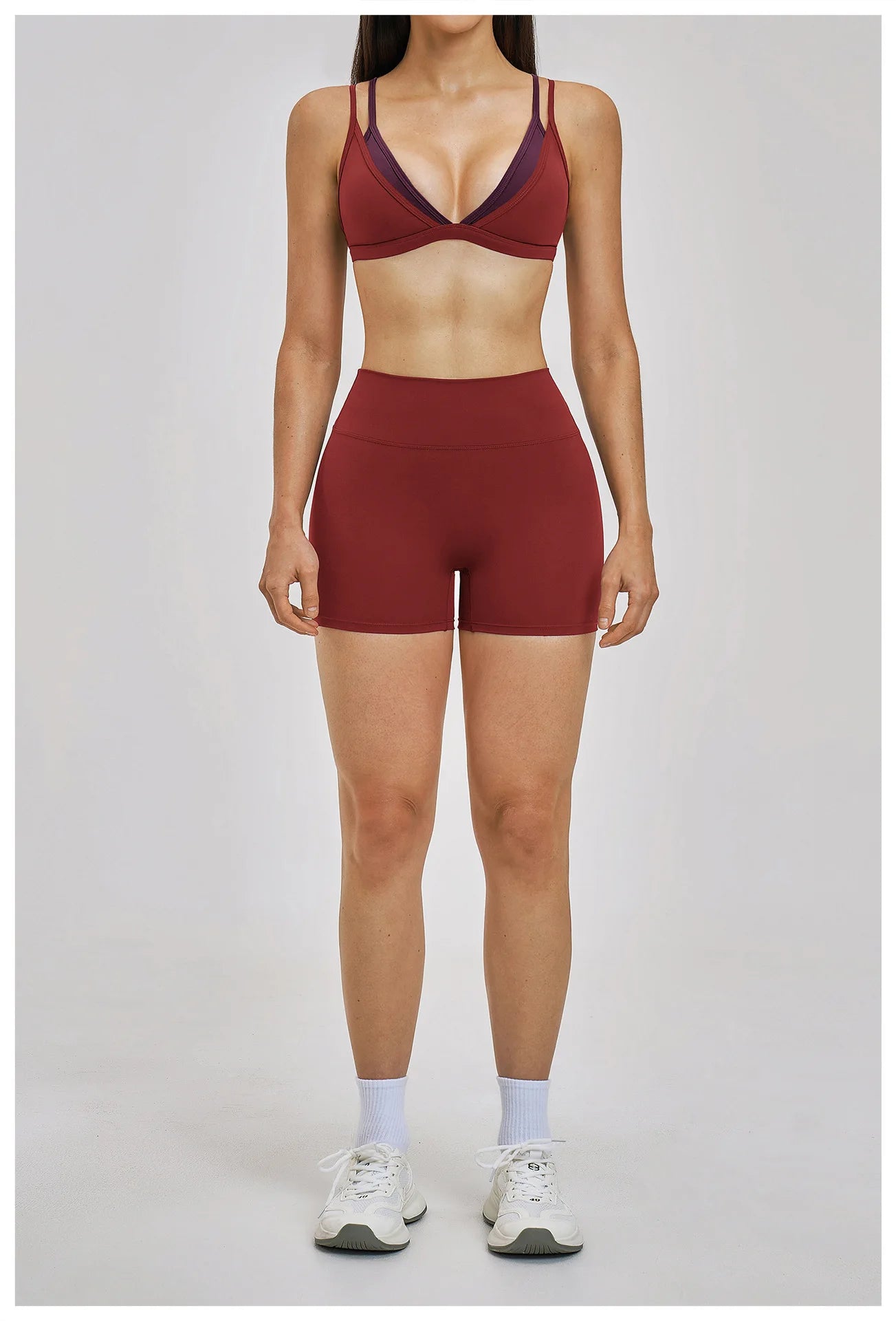 Person wearing a maroon sports bra and shorts set on a plain background